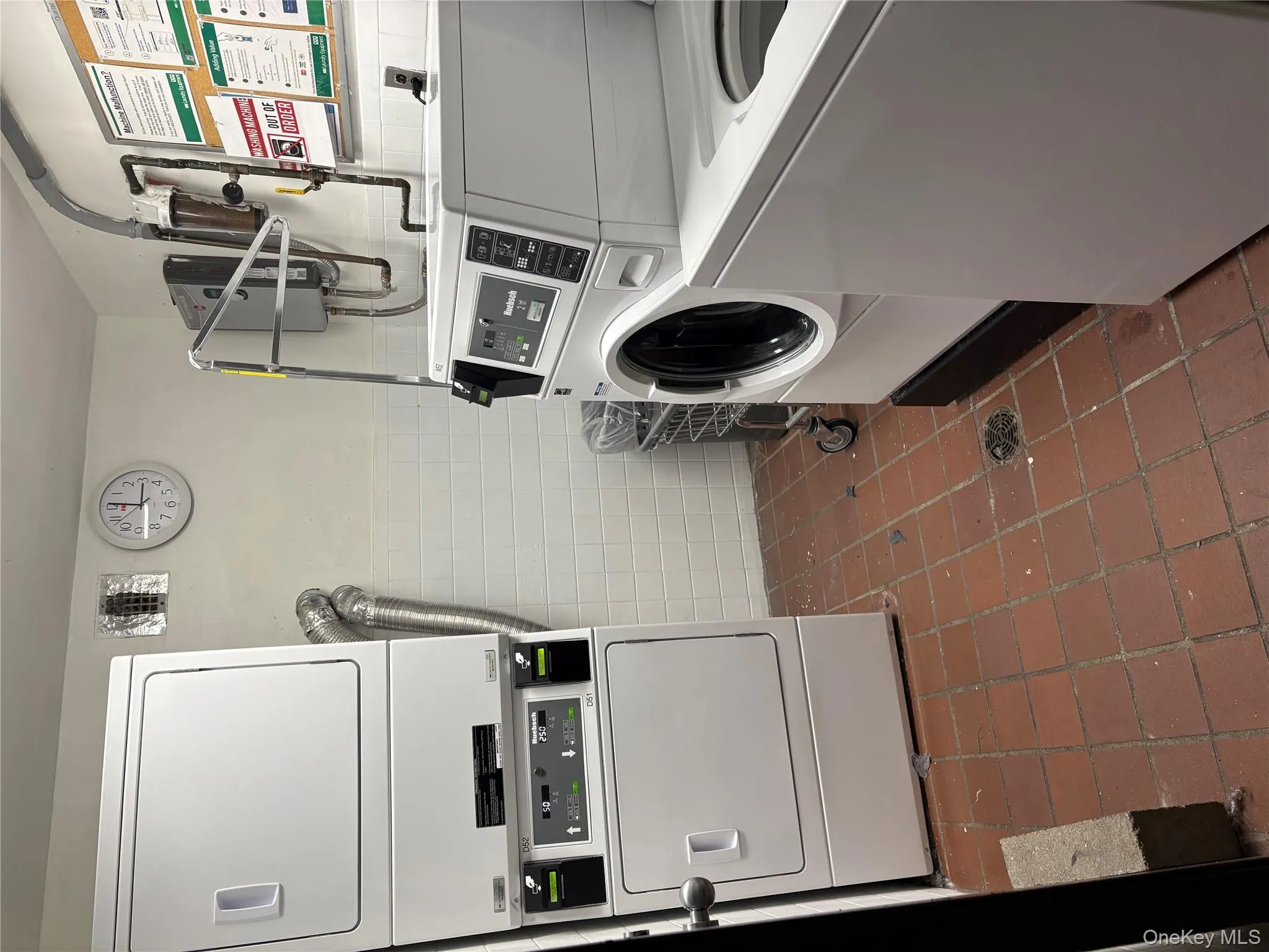 Shared laundry room featuring tile walls, a wainscoted wall, and stacked washer / drying machine Shared laundry room featuring tile walls, a wainscoted wall, and stacked washer / drying machine