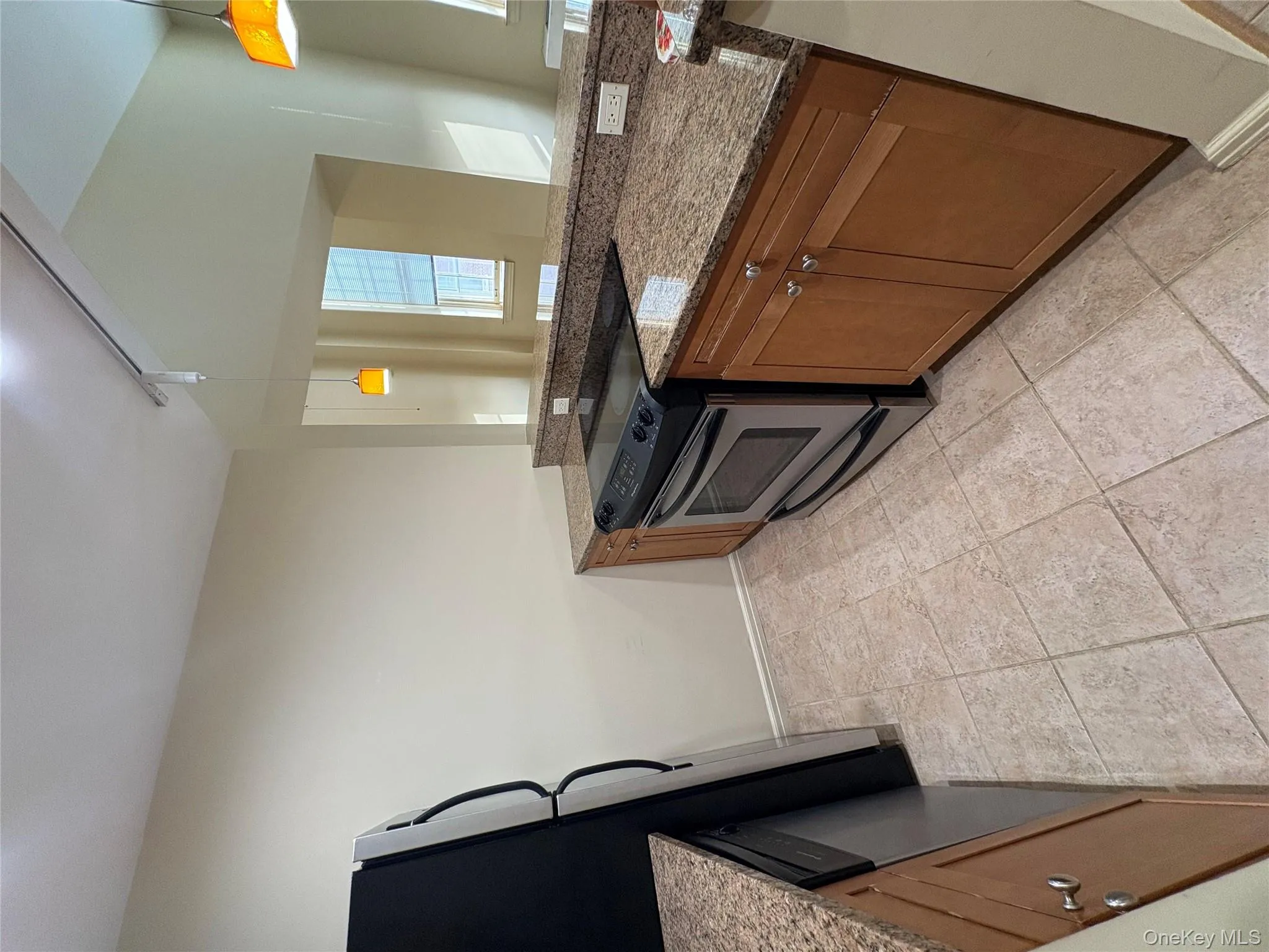 Kitchen with stainless steel range with electric stovetop, brown cabinetry, dark stone countertops, fridge, and decorative light fixtures Kitchen with stainless steel range with electric stovetop, brown cabinetry, dark stone countertops, fridge, and decorative light fixtures