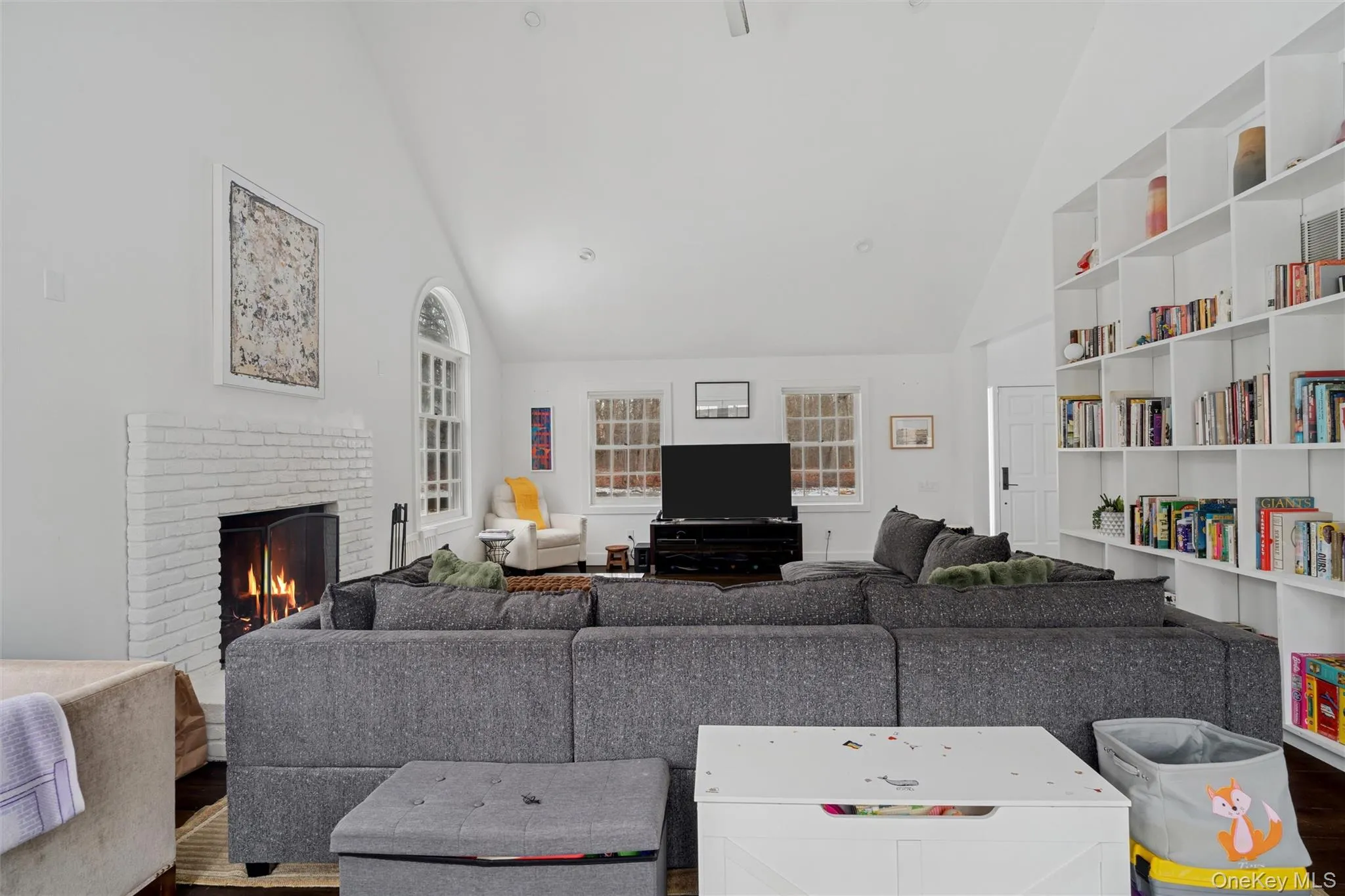 Living room with wood finished floors, high vaulted ceiling, a fireplace, and built in shelves Living room with wood finished floors, high vaulted ceiling, a fireplace, and built in shelves