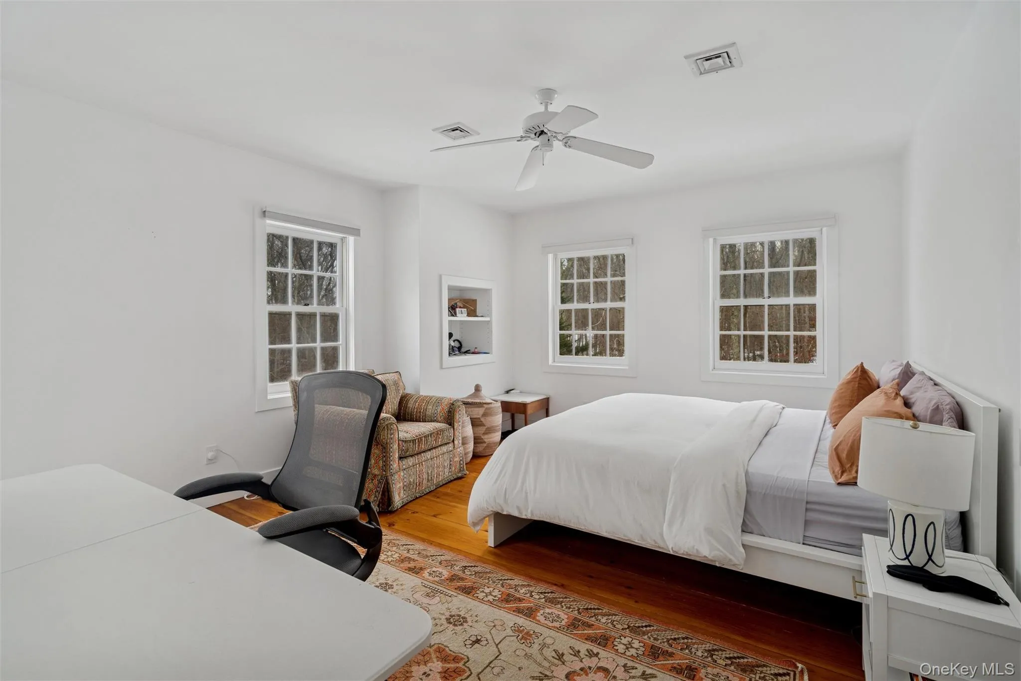 Bedroom with wood finished floors, a ceiling fan, an office area, and multiple windows Bedroom with wood finished floors, a ceiling fan, an office area, and multiple windows