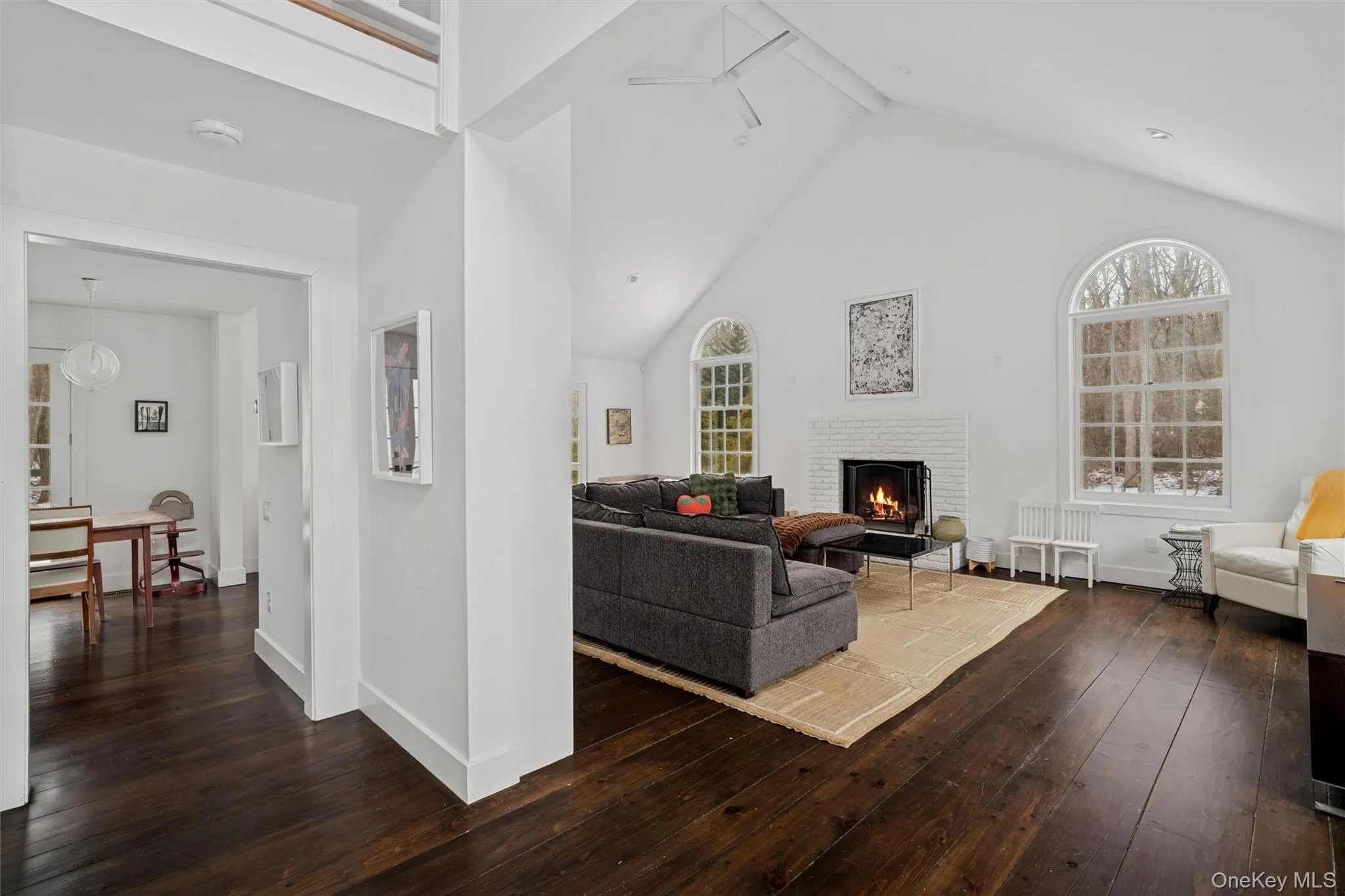 Living area with dark wood-type flooring, high vaulted ceiling, beamed ceiling, a fireplace, and a ceiling fan