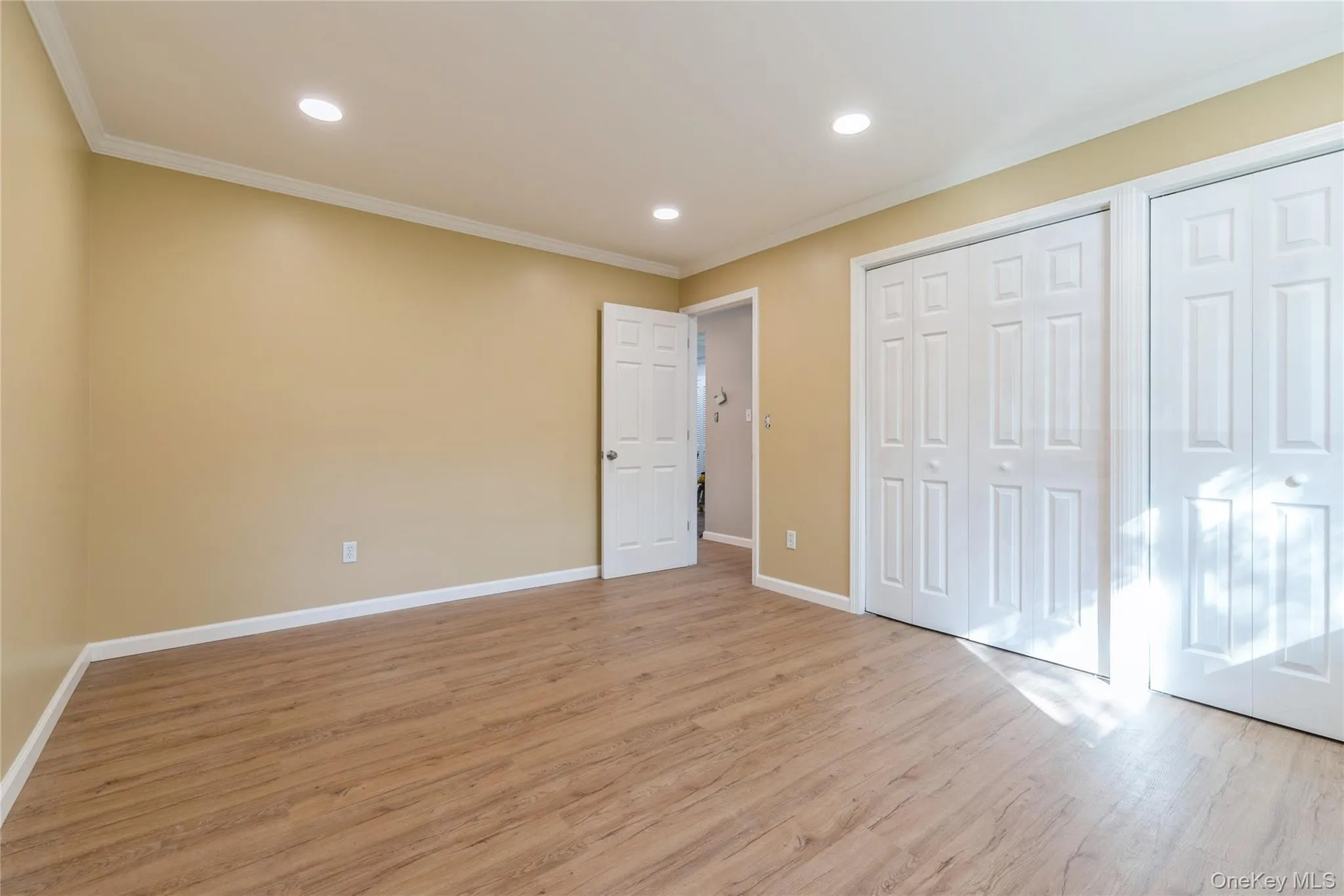 Unfurnished bedroom featuring multiple closets, light wood finished floors, ornamental molding, and recessed lighting Unfurnished bedroom featuring multiple closets, light wood finished floors, ornamental molding, and recessed lighting