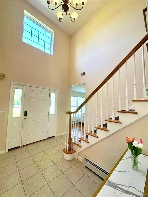 Entrance foyer with stairway, baseboard heating, a high ceiling, light tile patterned floors, and a chandelier Entrance foyer with stairway, baseboard heating, a high ceiling, light tile patterned floors, and a chandelier