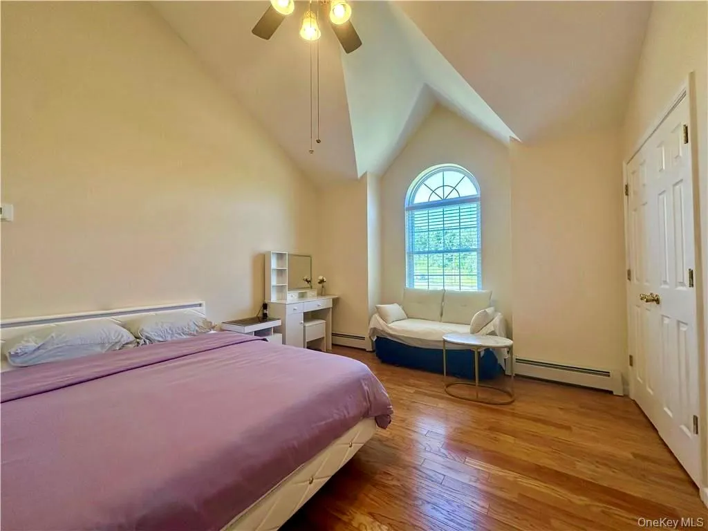 Bedroom featuring a baseboard heating unit, wood-type flooring, ceiling fan, and high vaulted ceiling Bedroom featuring a baseboard heating unit, wood-type flooring, ceiling fan, and high vaulted ceiling