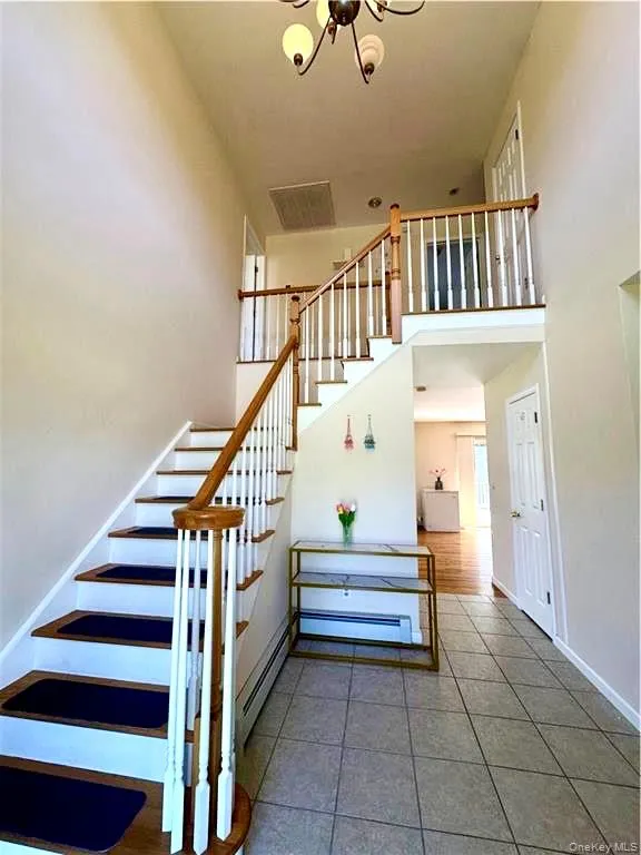 Staircase with tile patterned floors, a chandelier, a towering ceiling, and baseboard heating Staircase with tile patterned floors, a chandelier, a towering ceiling, and baseboard heating