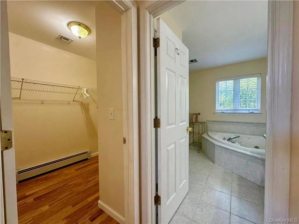 Full bathroom with baseboard heating, a garden tub, a spacious closet, and light tile patterned flooring Full bathroom with baseboard heating, a garden tub, a spacious closet, and light tile patterned flooring