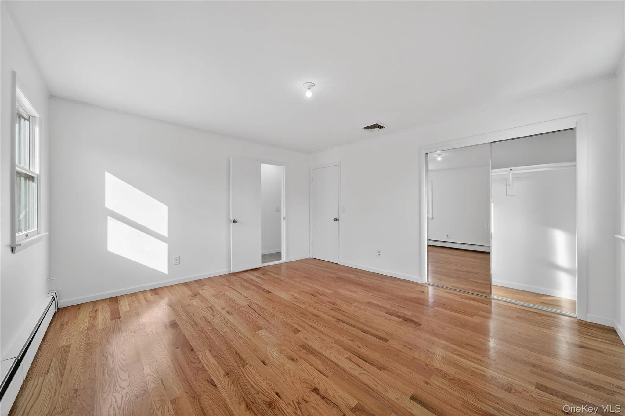 Unfurnished bedroom featuring baseboard heating and light wood-style flooring Unfurnished bedroom featuring baseboard heating and light wood-style flooring