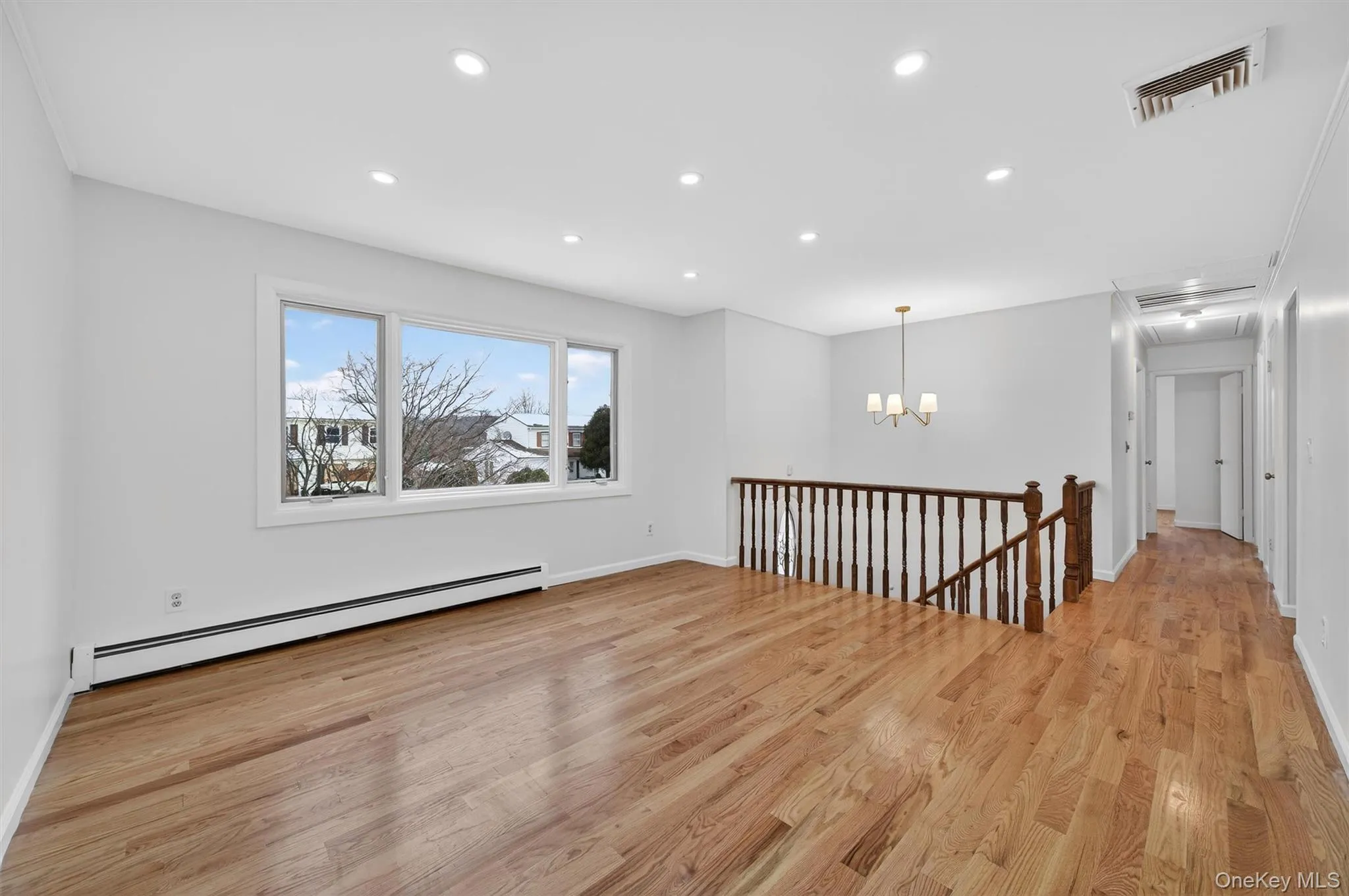 Empty room with a baseboard radiator, recessed lighting, light wood finished floors, and a chandelier Empty room with a baseboard radiator, recessed lighting, light wood finished floors, and a chandelier