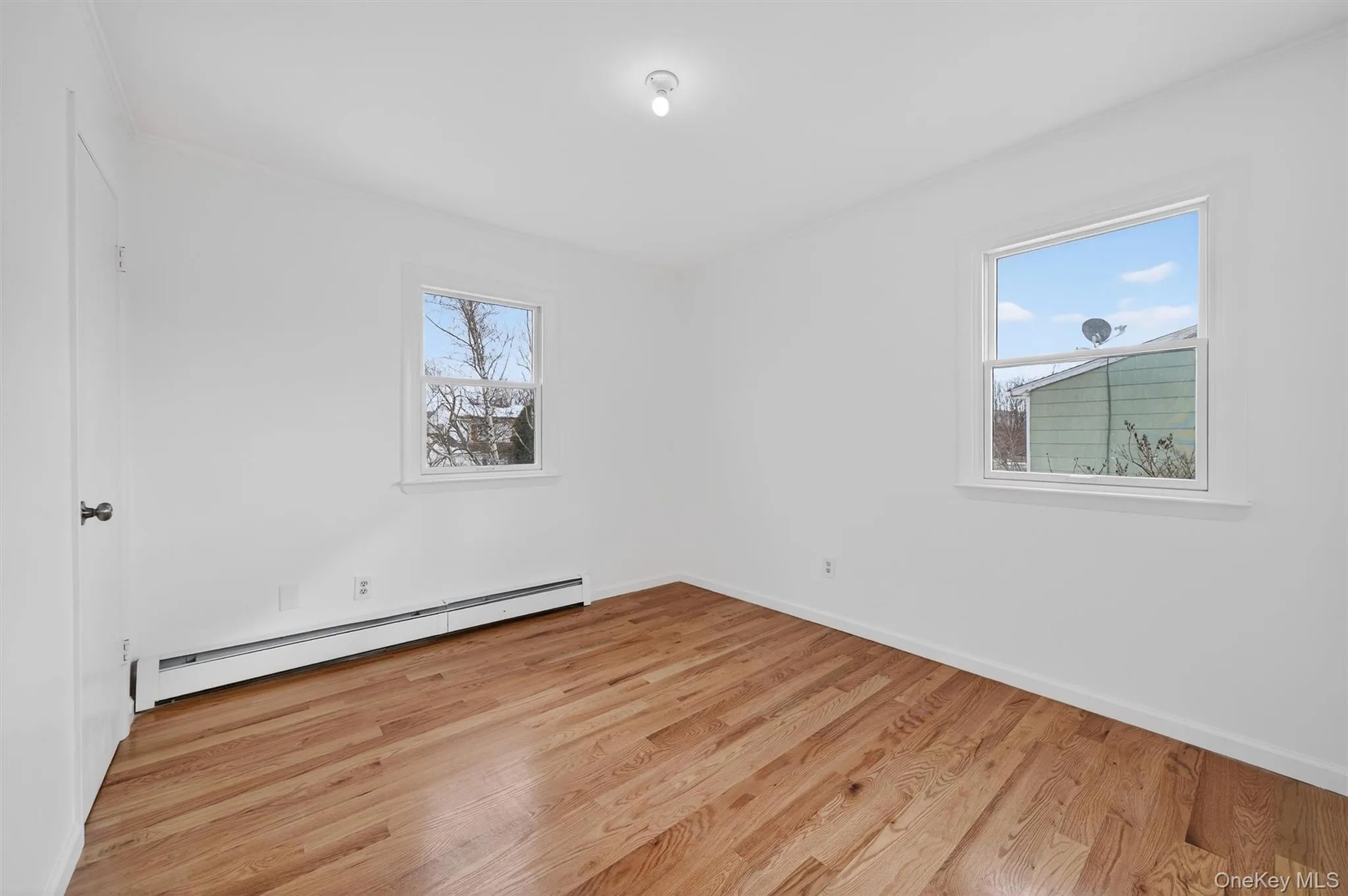 Spare room with baseboard heating, light wood-type flooring, healthy amount of natural light, and ornamental molding Spare room with baseboard heating, light wood-type flooring, healthy amount of natural light, and ornamental molding