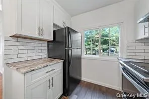Kitchen with decorative backsplash, white cabinetry, freestanding refrigerator, dark wood finished floors, and stainless steel range oven Kitchen with decorative backsplash, white cabinetry, freestanding refrigerator, dark wood finished floors, and stainless steel range oven