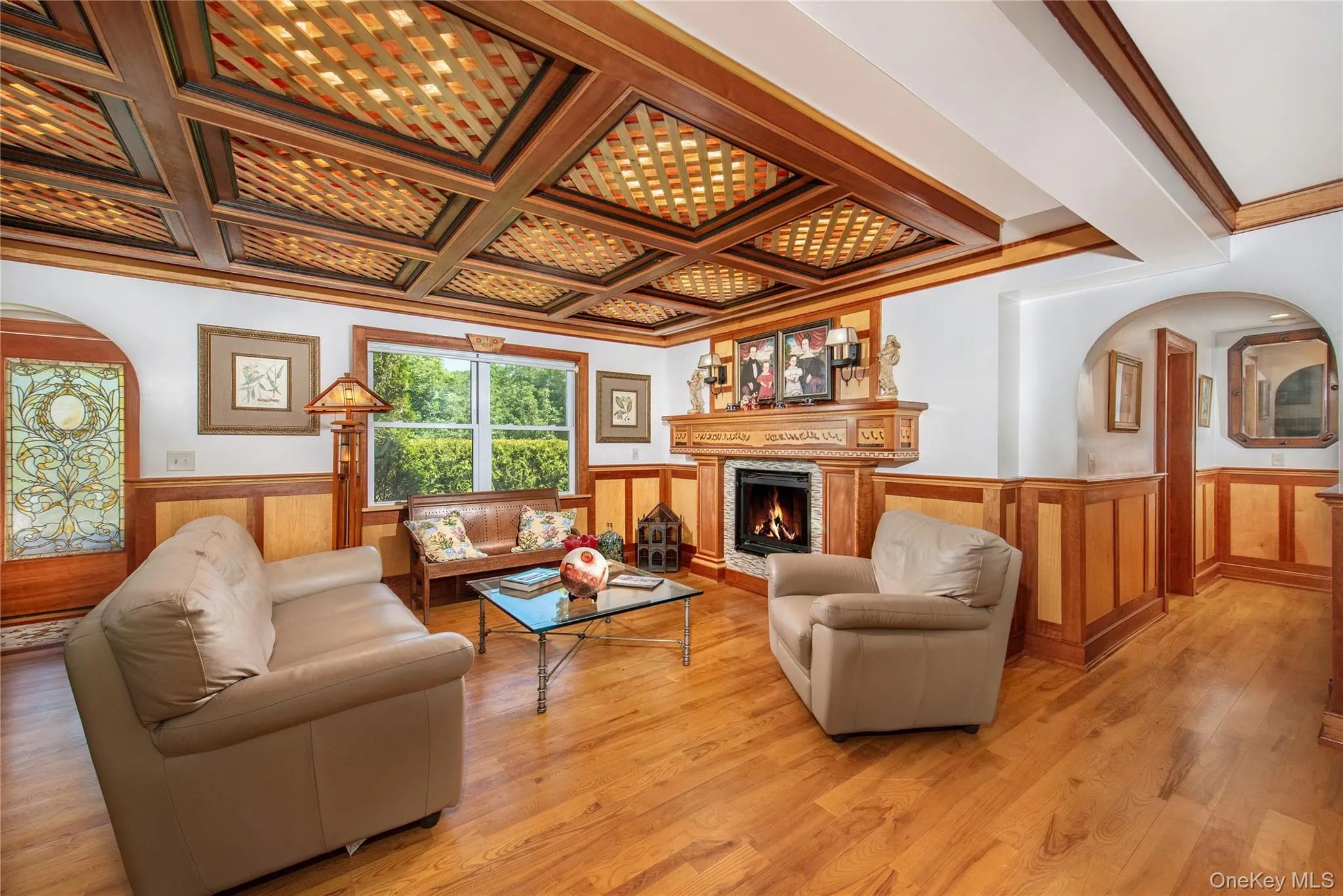 Living area with wainscoting, arched walkways, a fireplace, crown molding, and coffered ceiling Living area with wainscoting, arched walkways, a fireplace, crown molding, and coffered ceiling