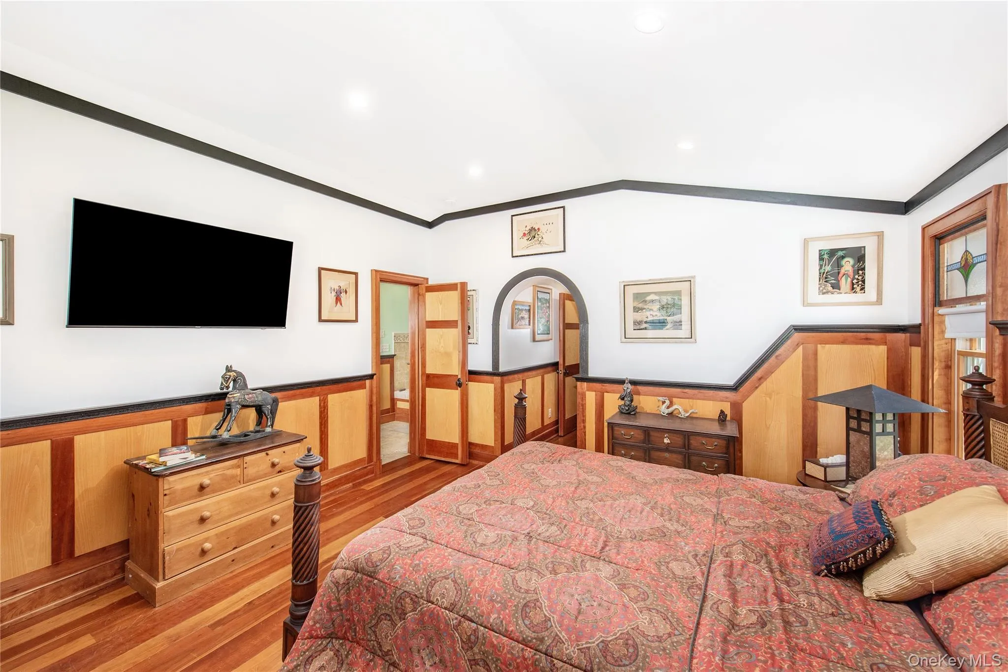 Bedroom with a wainscoted wall, light wood-style flooring, ornamental molding, and vaulted ceiling Bedroom with a wainscoted wall, light wood-style flooring, ornamental molding, and vaulted ceiling