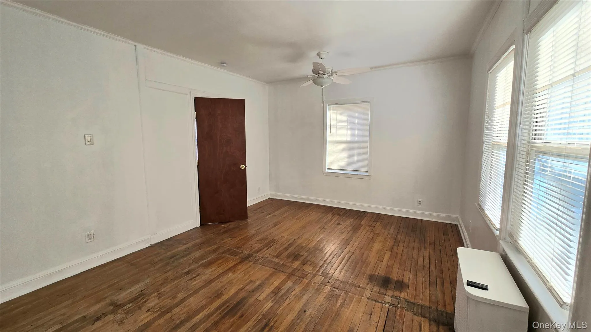 Empty room featuring dark wood-type flooring, a ceiling fan, and ornamental molding Empty room featuring dark wood-type flooring, a ceiling fan, and ornamental molding