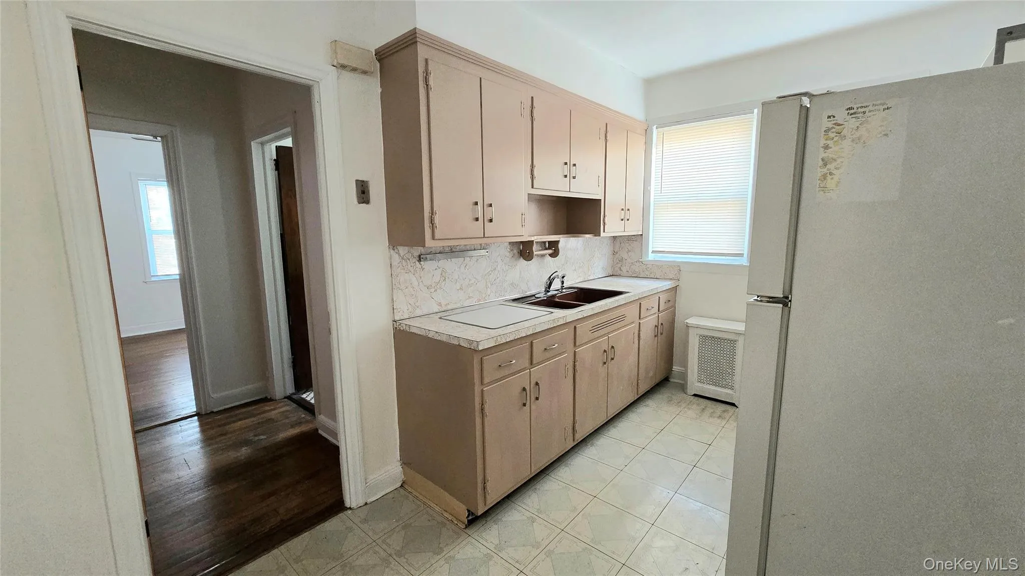 Kitchen featuring freestanding refrigerator, light countertops, tasteful backsplash, light tile patterned floors, and radiator Kitchen featuring freestanding refrigerator, light countertops, tasteful backsplash, light tile patterned floors, and radiator