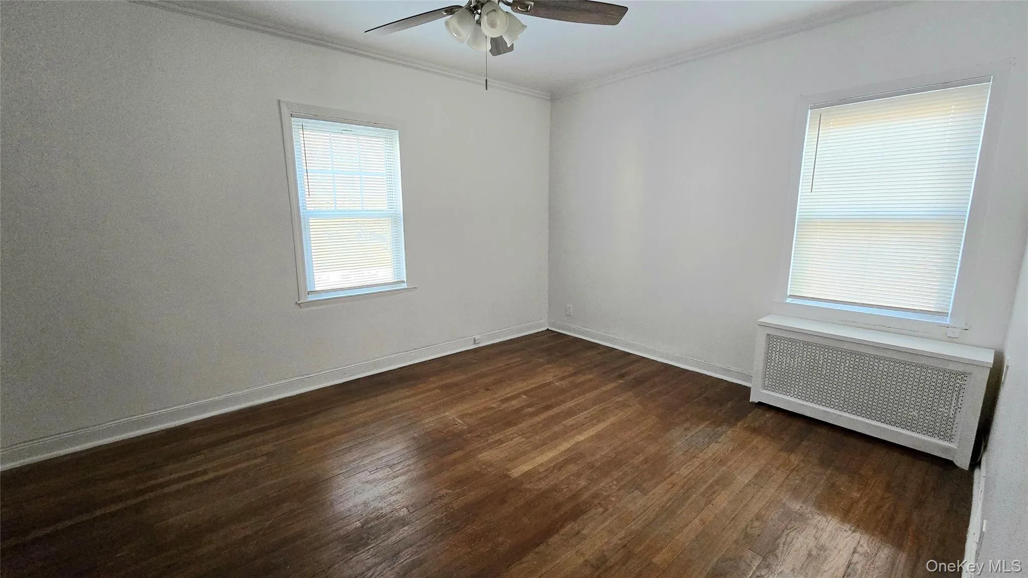 Empty room with radiator heating unit, ornamental molding, dark wood finished floors, and a ceiling fan Empty room with radiator heating unit, ornamental molding, dark wood finished floors, and a ceiling fan