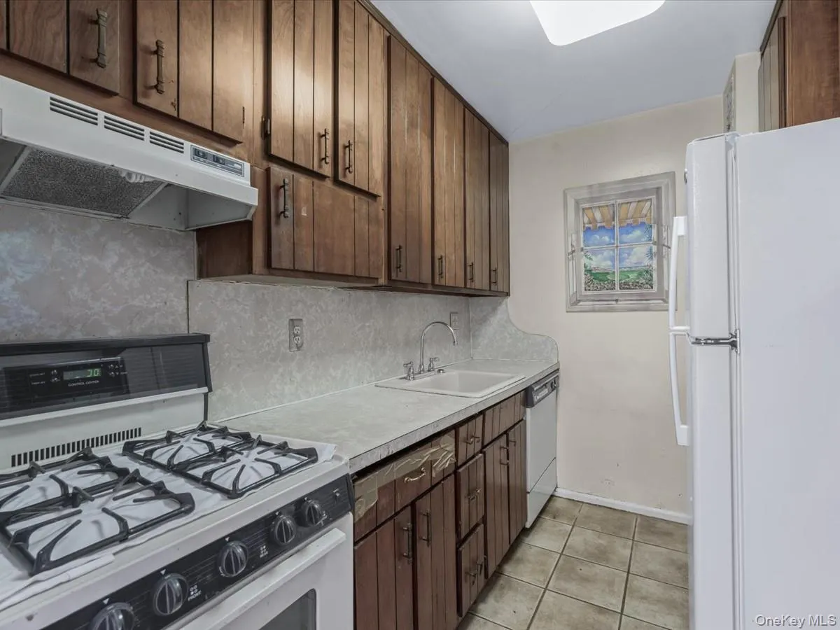 Kitchen featuring white appliances, under cabinet range hood, dark brown cabinetry, light tile patterned floors, and light countertops Kitchen featuring white appliances, under cabinet range hood, dark brown cabinetry, light tile patterned floors, and light countertops
