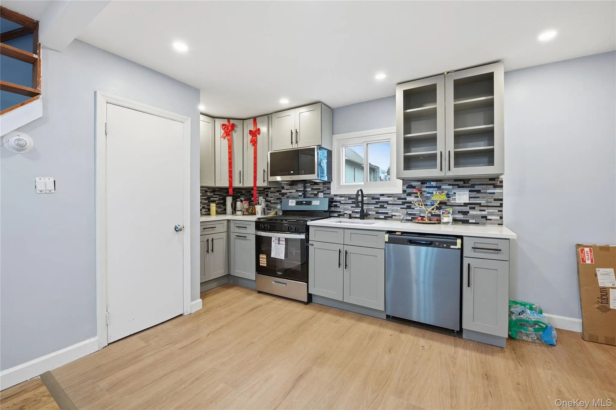 Kitchen with gray cabinetry, stainless steel appliances, glass insert cabinets, light wood finished floors, and recessed lighting Kitchen with gray cabinetry, stainless steel appliances, glass insert cabinets, light wood finished floors, and recessed lighting