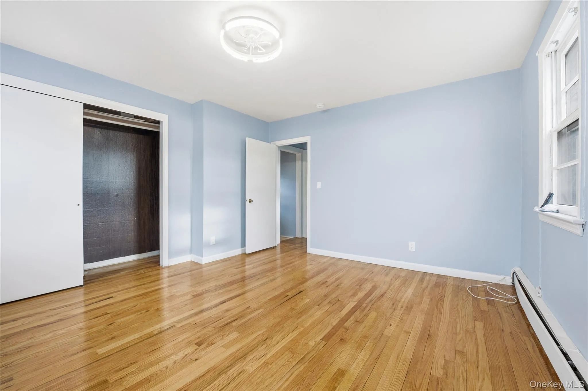 Unfurnished bedroom featuring baseboard heating, a closet, and light wood-style floors Unfurnished bedroom featuring baseboard heating, a closet, and light wood-style floors