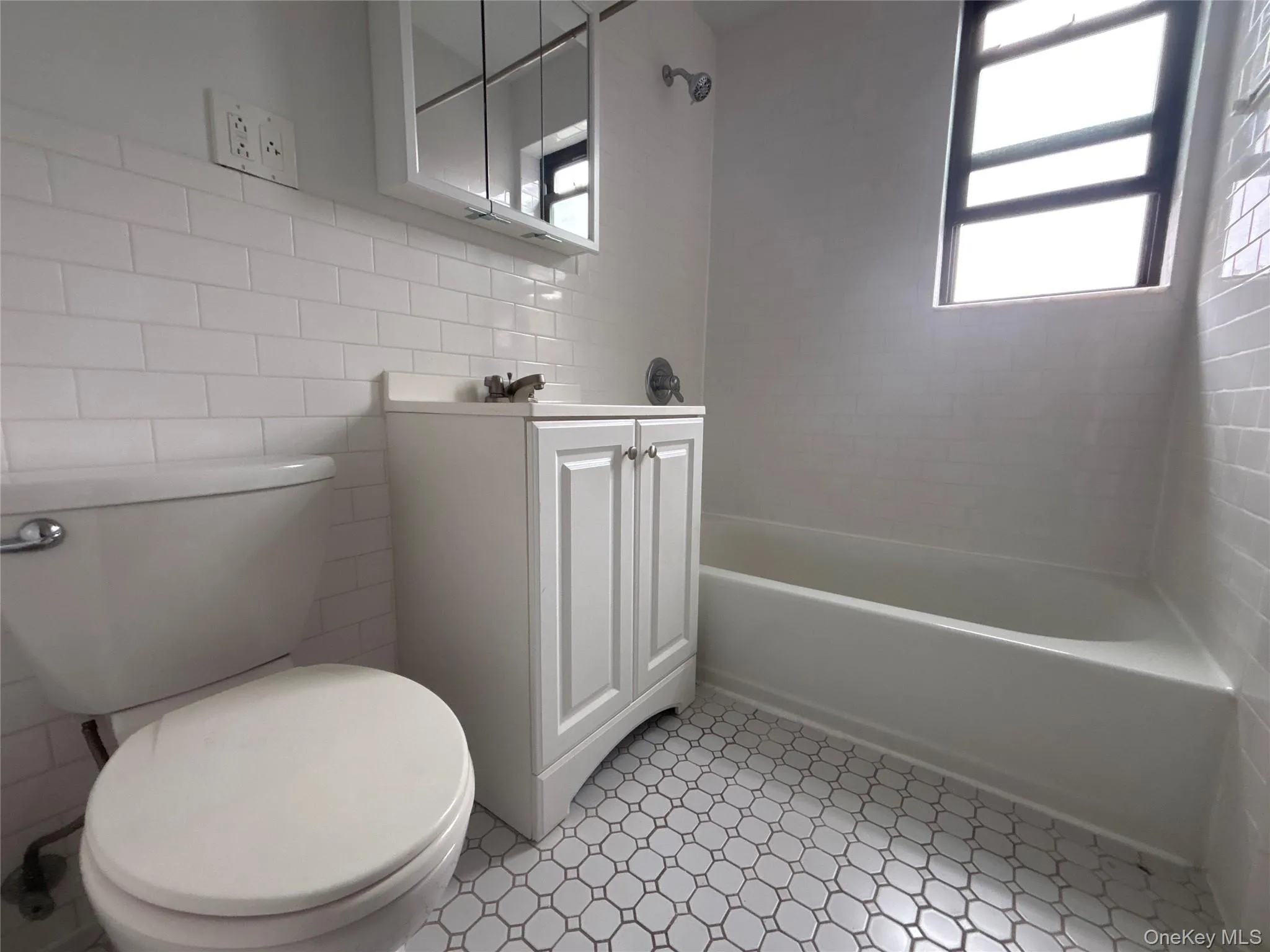Bathroom with tile walls, vanity, washtub / shower combination, and healthy amount of natural light Bathroom with tile walls, vanity, washtub / shower combination, and healthy amount of natural light