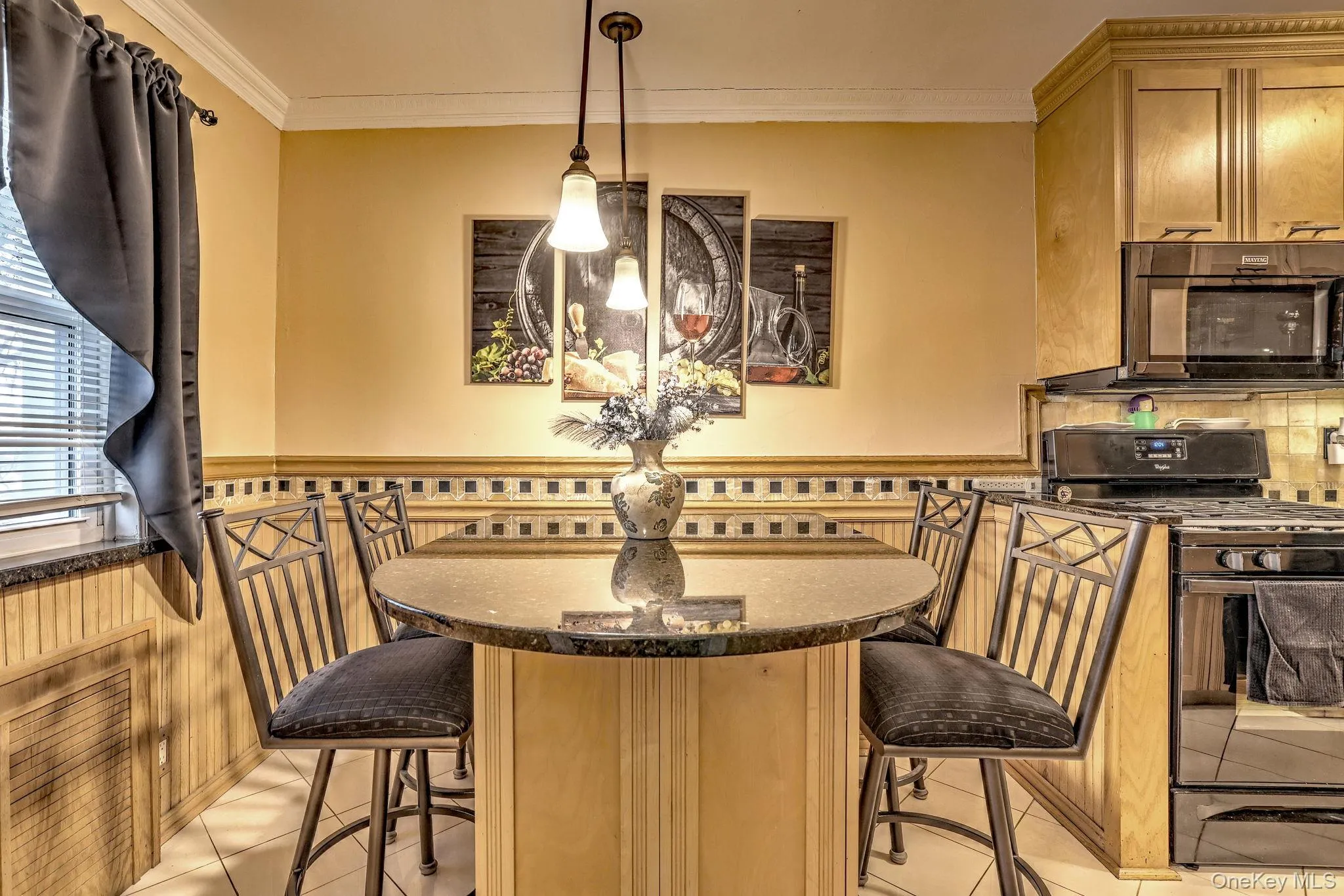 Kitchen with black appliances, a breakfast bar area, wainscoting, dark stone countertops, and decorative light fixtures Kitchen with black appliances, a breakfast bar area, wainscoting, dark stone countertops, and decorative light fixtures