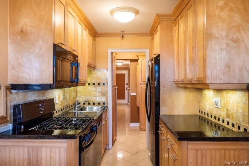 Kitchen with black appliances, tasteful backsplash, light tile patterned floors, ornamental molding, and dark stone countertops Kitchen with black appliances, tasteful backsplash, light tile patterned floors, ornamental molding, and dark stone countertops