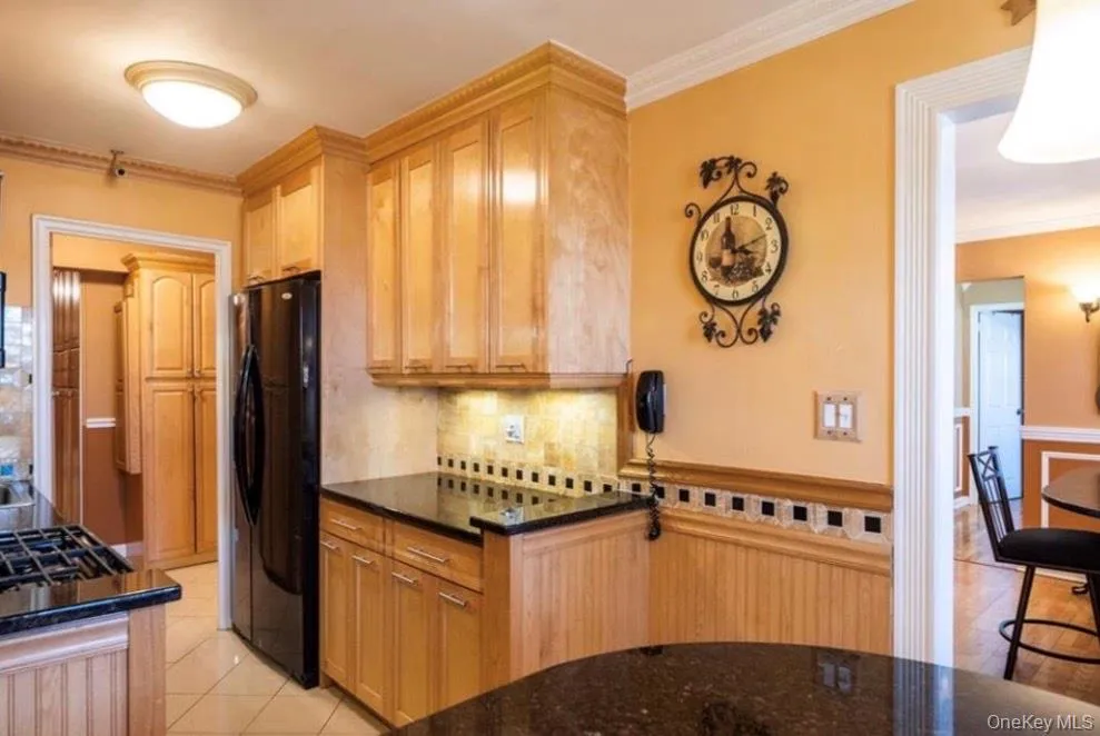 Kitchen featuring ornamental molding, freestanding refrigerator, light tile patterned floors, tasteful backsplash, and dark stone counters Kitchen featuring ornamental molding, freestanding refrigerator, light tile patterned floors, tasteful backsplash, and dark stone counters