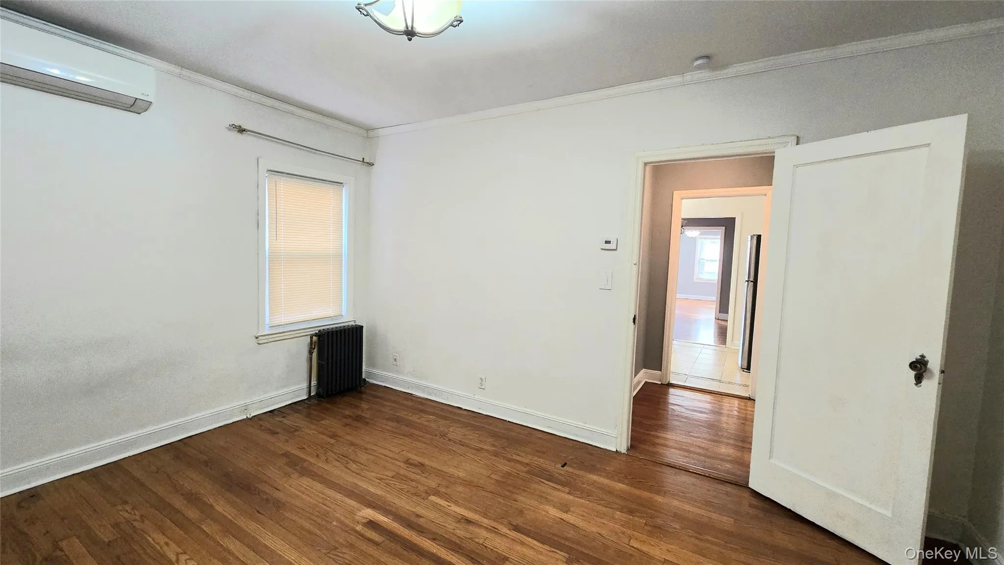 Spare room with crown molding, an AC wall unit, radiator heating unit, and dark wood-type flooring Spare room with crown molding, an AC wall unit, radiator heating unit, and dark wood-type flooring