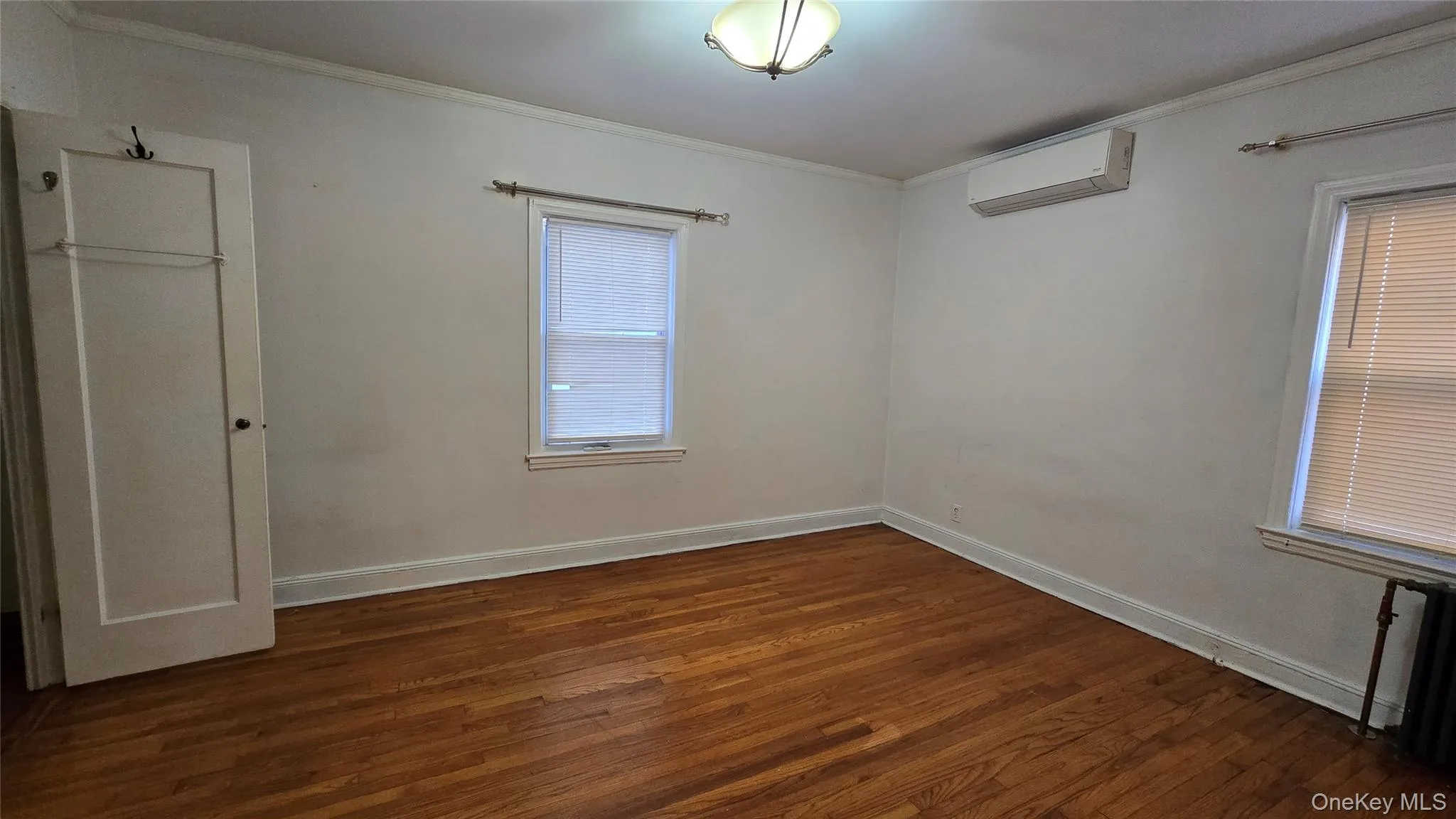 Unfurnished bedroom with crown molding, dark wood-type flooring, and a wall mounted AC Unfurnished bedroom with crown molding, dark wood-type flooring, and a wall mounted AC