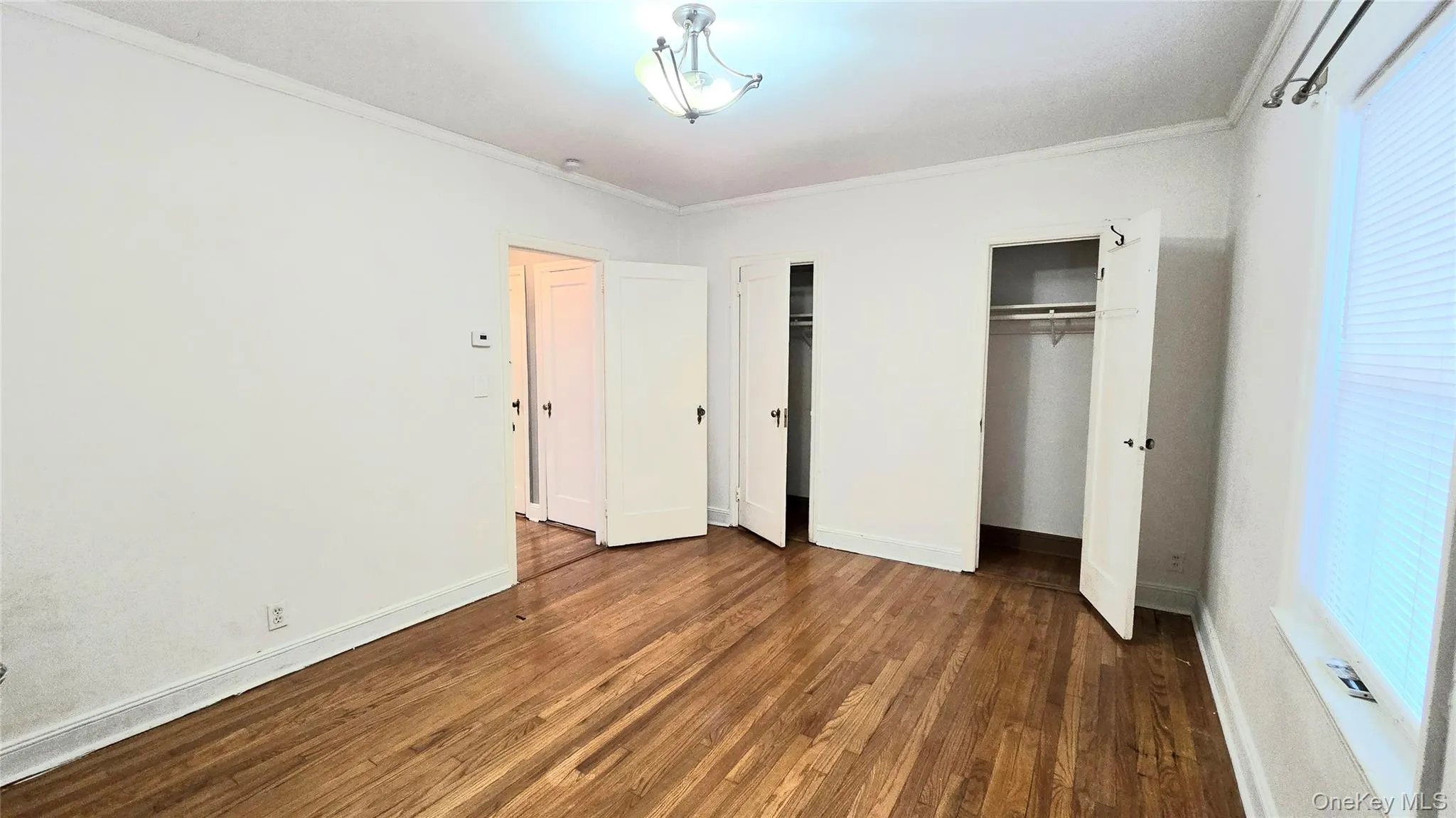 Unfurnished bedroom with multiple closets, crown molding, and dark wood-type flooring Unfurnished bedroom with multiple closets, crown molding, and dark wood-type flooring