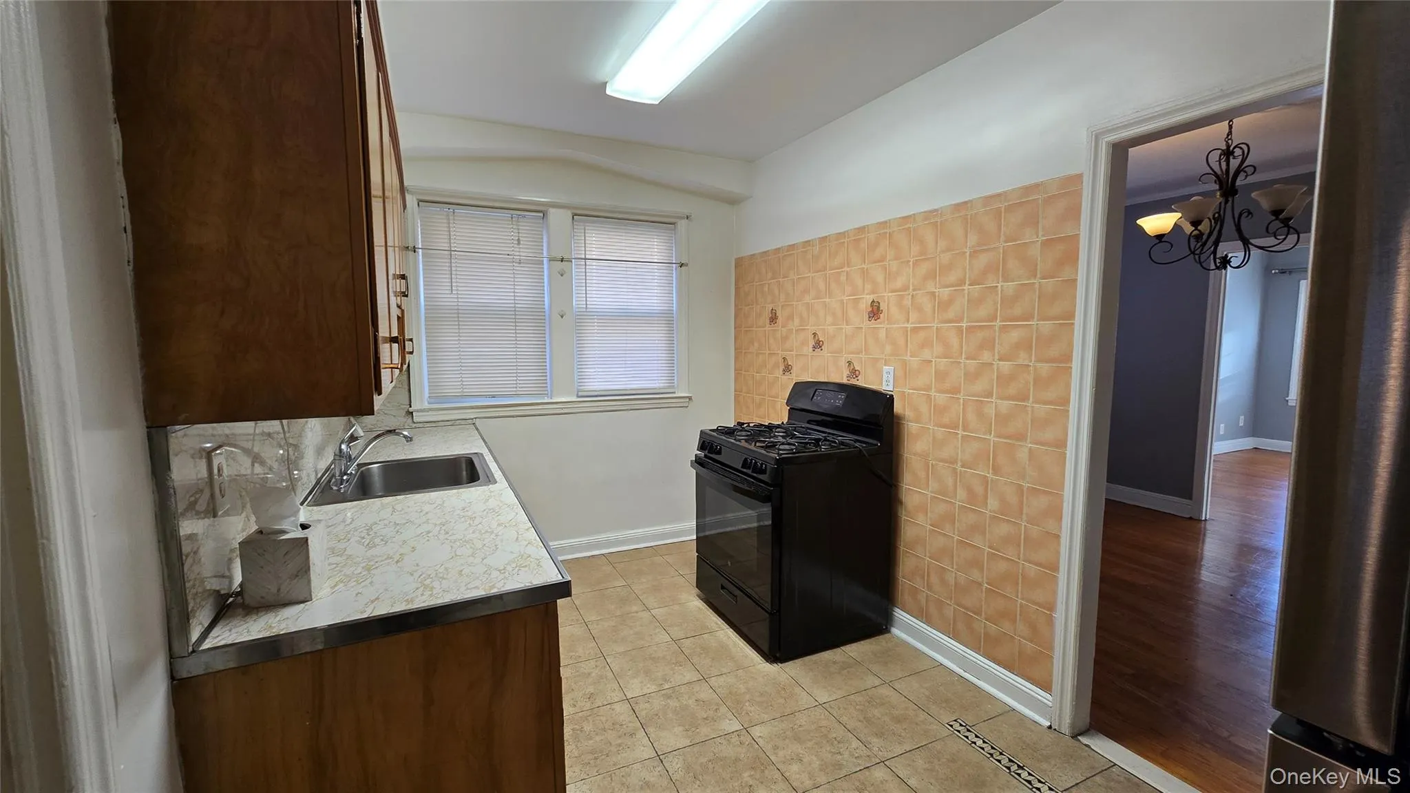 Kitchen featuring black range with gas stovetop, light tile patterned flooring, light countertops, a chandelier, and stainless steel fridge Kitchen featuring black range with gas stovetop, light tile patterned flooring, light countertops, a chandelier, and stainless steel fridge