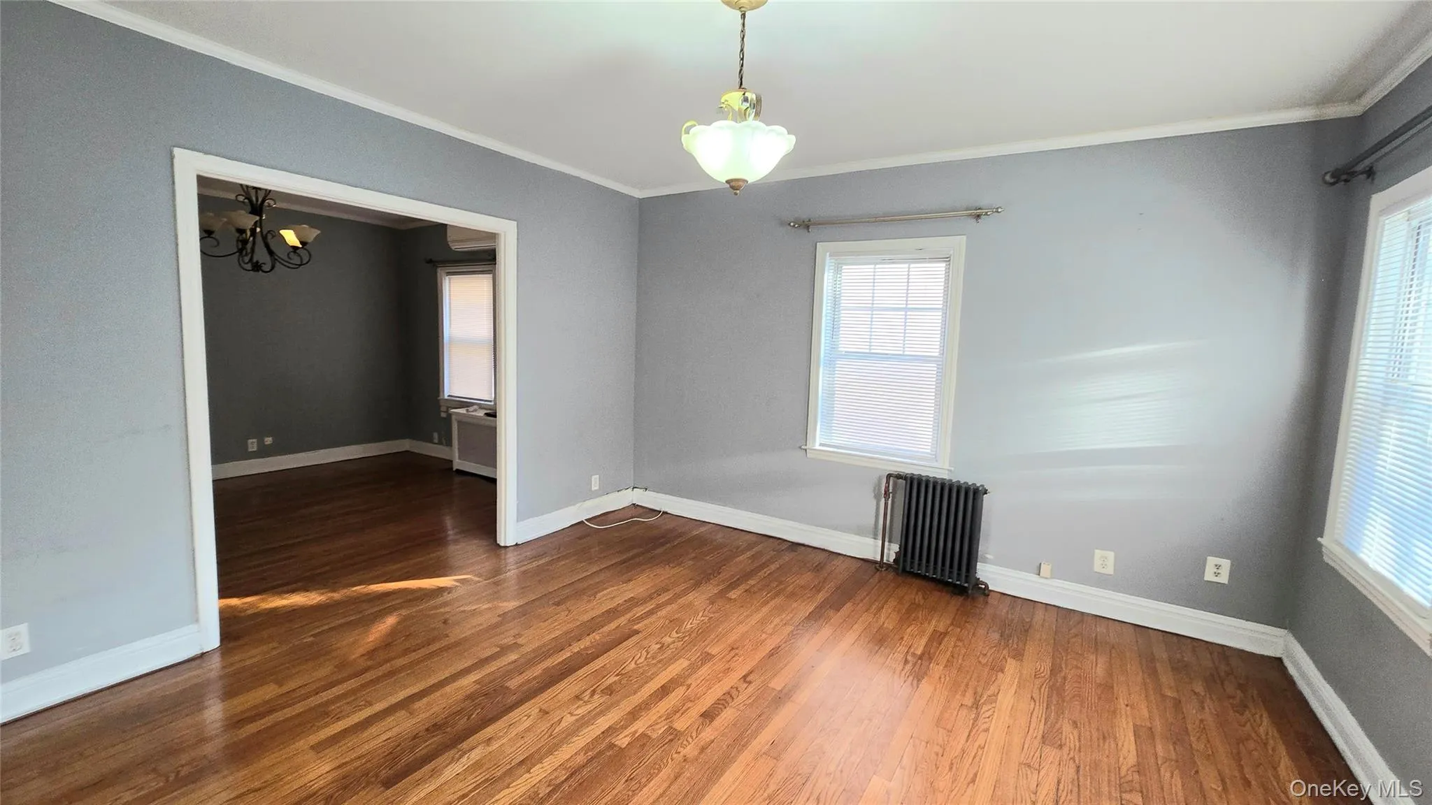 Unfurnished room featuring crown molding, radiator, a chandelier, and dark wood-style floors Unfurnished room featuring crown molding, radiator, a chandelier, and dark wood-style floors