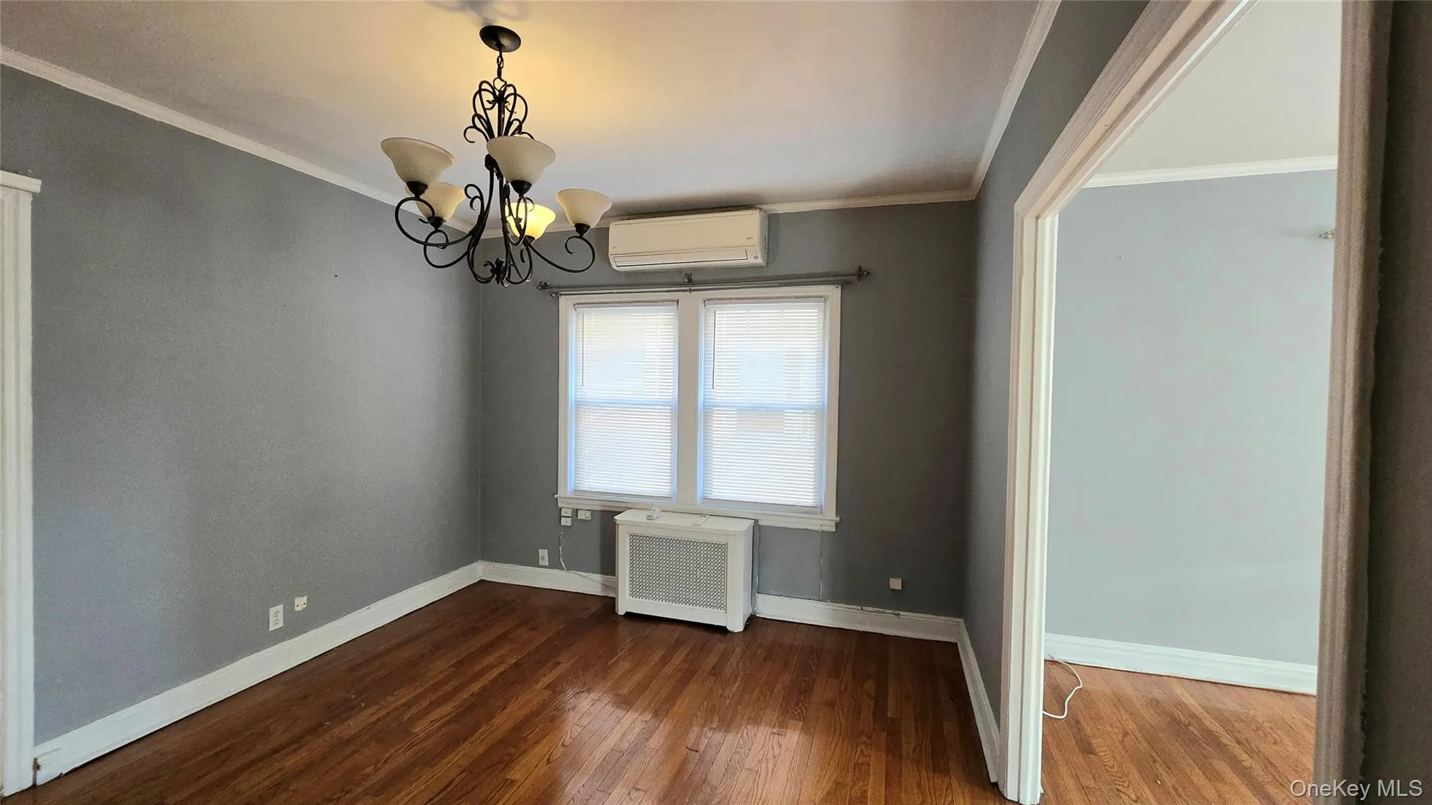 Unfurnished dining area with radiator, a wall unit AC, crown molding, dark wood-style flooring, and a chandelier Unfurnished dining area with radiator, a wall unit AC, crown molding, dark wood-style flooring, and a chandelier