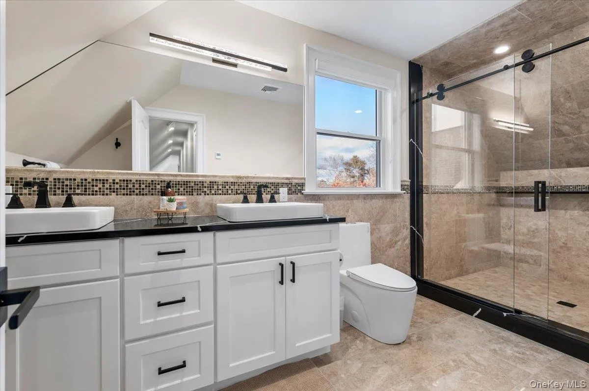Bathroom with double vanity, a stall shower, and tile walls Bathroom with double vanity, a stall shower, and tile walls