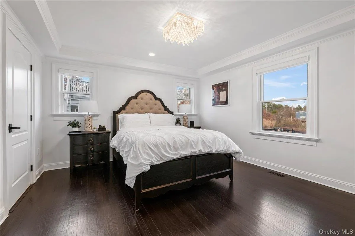 Bedroom featuring crown molding, dark wood-type flooring, a chandelier, a tray ceiling, and recessed lighting Bedroom featuring crown molding, dark wood-type flooring, a chandelier, a tray ceiling, and recessed lighting