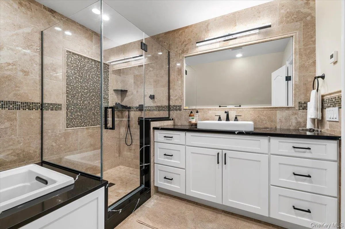 Bathroom with tile walls, vanity, a stall shower, recessed lighting, and a bathtub Bathroom with tile walls, vanity, a stall shower, recessed lighting, and a bathtub