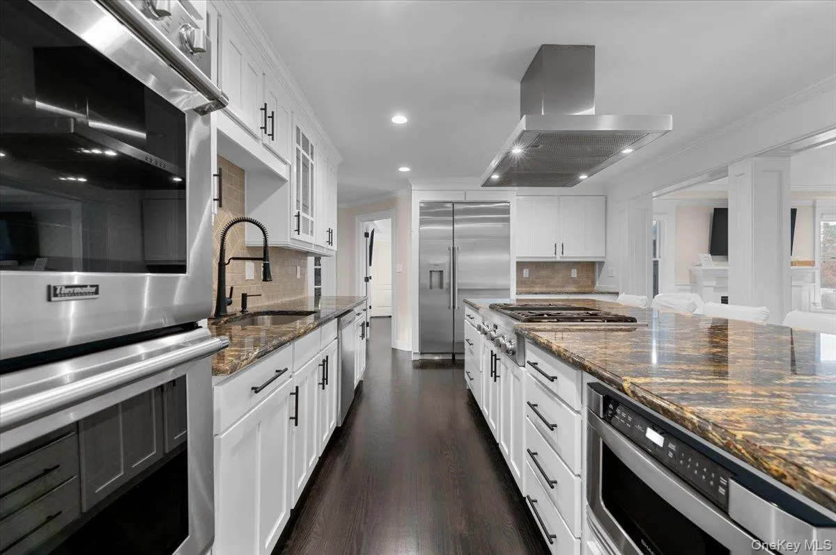 Kitchen with appliances with stainless steel finishes, crown molding, dark stone counters, extractor fan, and white cabinetry Kitchen with appliances with stainless steel finishes, crown molding, dark stone counters, extractor fan, and white cabinetry