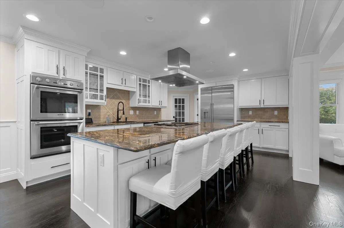 Kitchen featuring ornamental molding, white cabinetry, dark stone countertops, a kitchen breakfast bar, and glass insert cabinets Kitchen featuring ornamental molding, white cabinetry, dark stone countertops, a kitchen breakfast bar, and glass insert cabinets