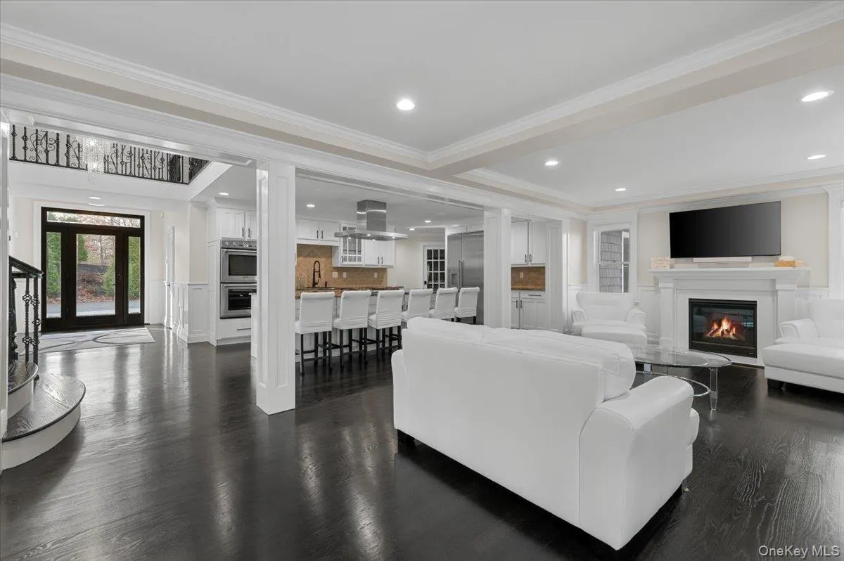 Living room featuring a glass covered fireplace, recessed lighting, dark wood-style flooring, ornamental molding, and stairs Living room featuring a glass covered fireplace, recessed lighting, dark wood-style flooring, ornamental molding, and stairs