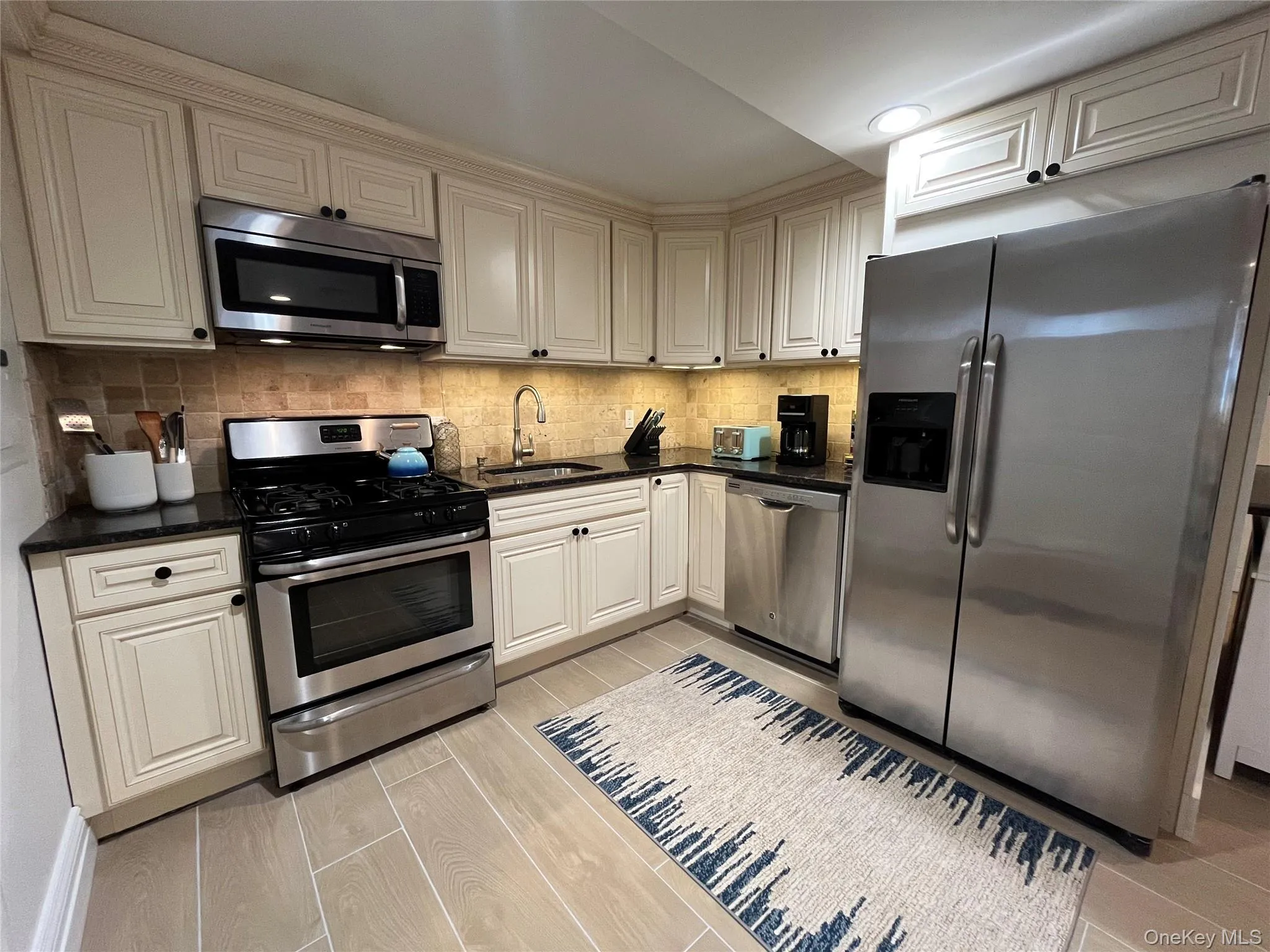 Kitchen featuring stainless steel appliances, cream cabinets, dark stone counters, and decorative backsplash Kitchen featuring stainless steel appliances, cream cabinets, dark stone counters, and decorative backsplash