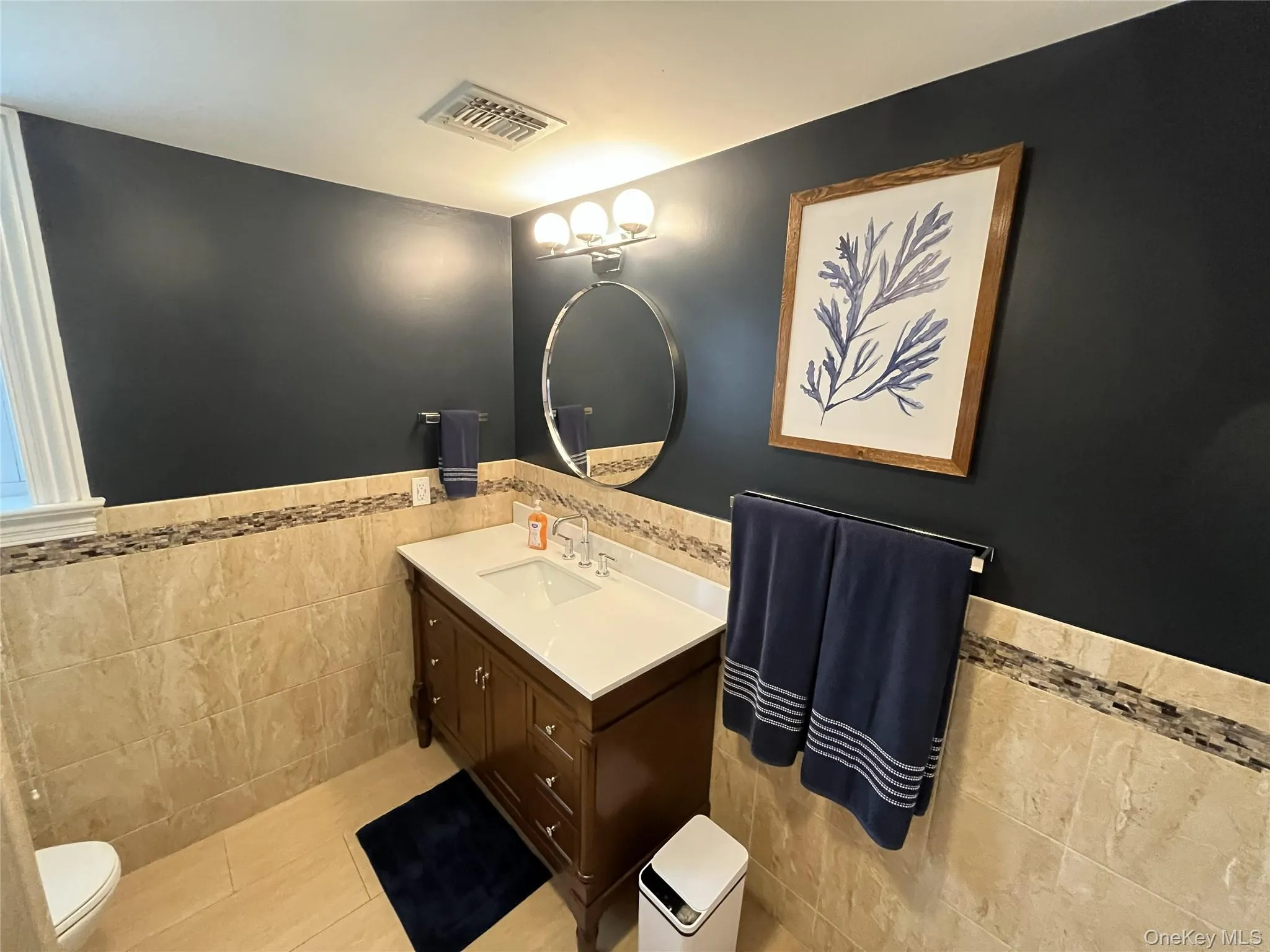 Bathroom with wainscoting, tile walls, vanity, and light tile patterned floors Bathroom with wainscoting, tile walls, vanity, and light tile patterned floors