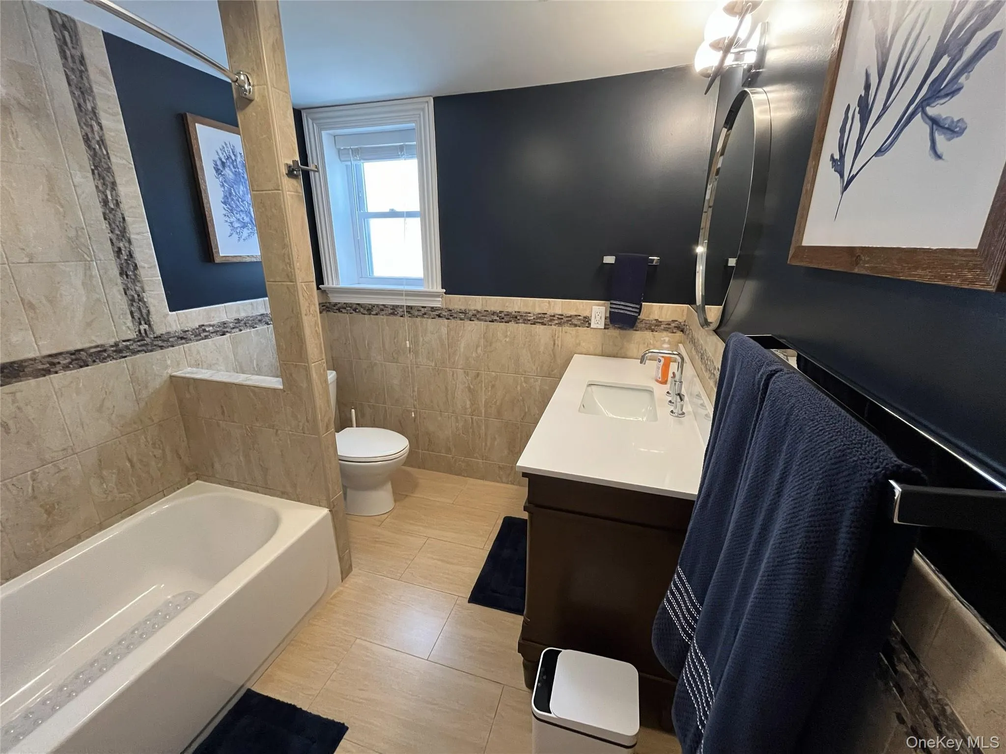 Full bath with vanity, tile walls, a wainscoted wall, shower / washtub combination, and light tile patterned floors Full bath with vanity, tile walls, a wainscoted wall, shower / washtub combination, and light tile patterned floors