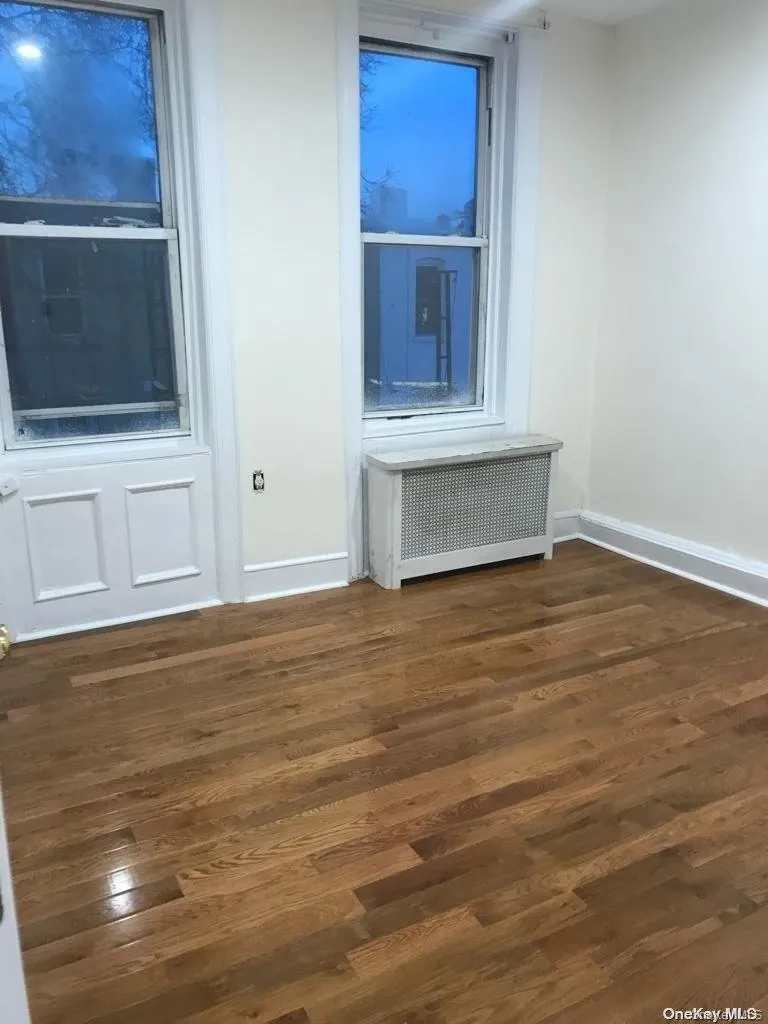 Empty room featuring dark wood-style flooring and radiator heating unit Empty room featuring dark wood-style flooring and radiator heating unit