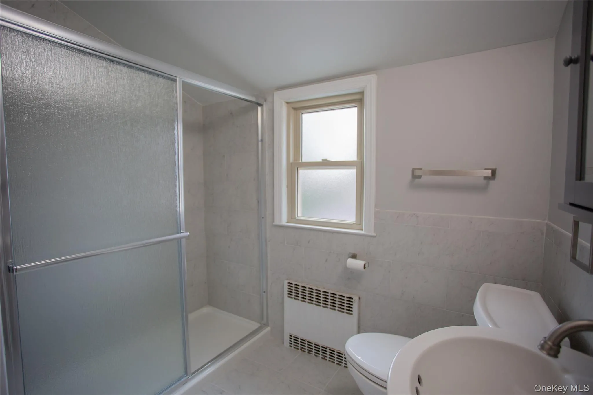 Full bath with radiator heating unit, tile walls, wainscoting, a shower stall, and tile patterned floors Full bath with radiator heating unit, tile walls, wainscoting, a shower stall, and tile patterned floors
