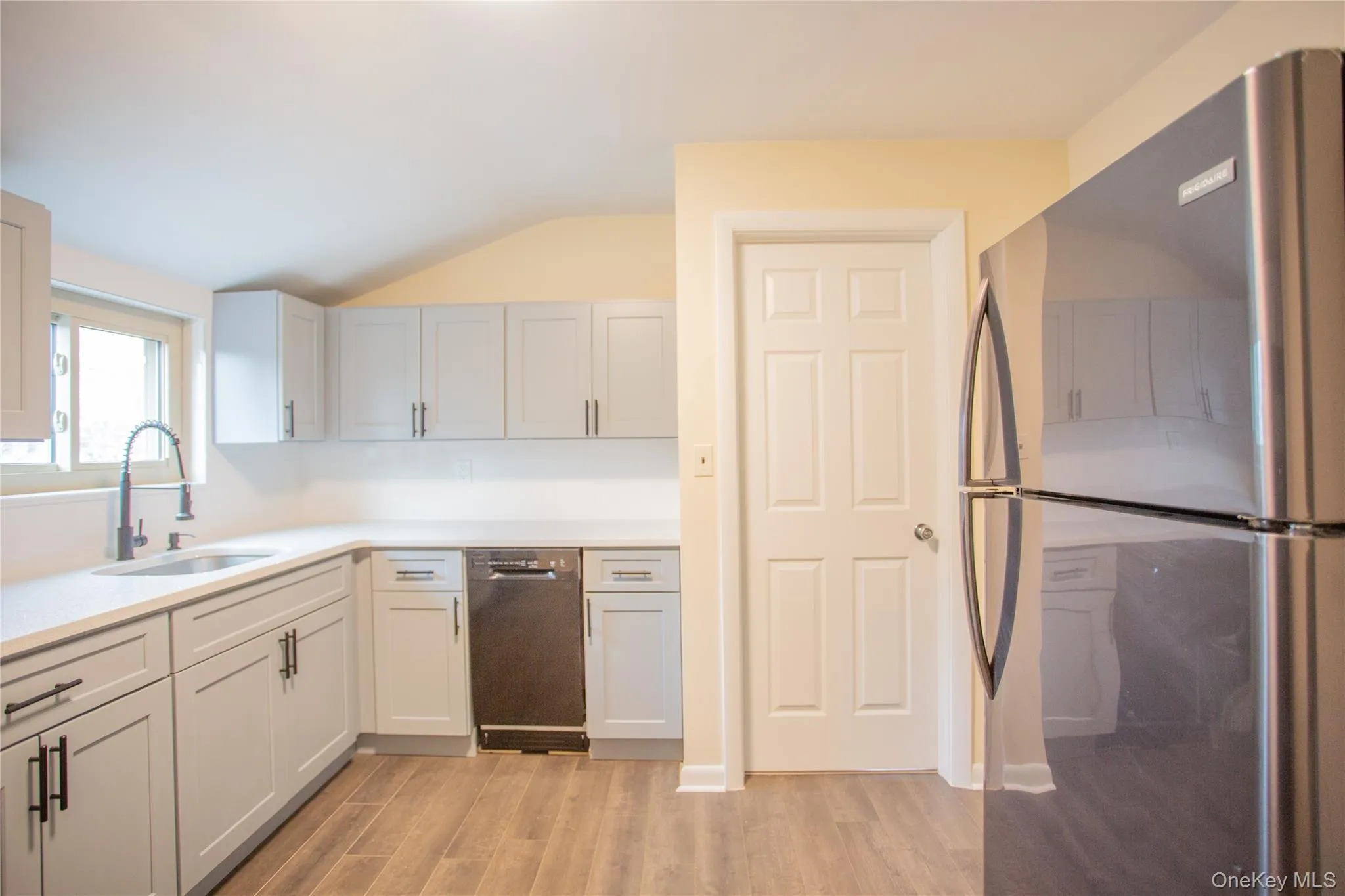 Kitchen with freestanding refrigerator, vaulted ceiling, light wood finished floors, dishwasher, and light stone countertops Kitchen with freestanding refrigerator, vaulted ceiling, light wood finished floors, dishwasher, and light stone countertops