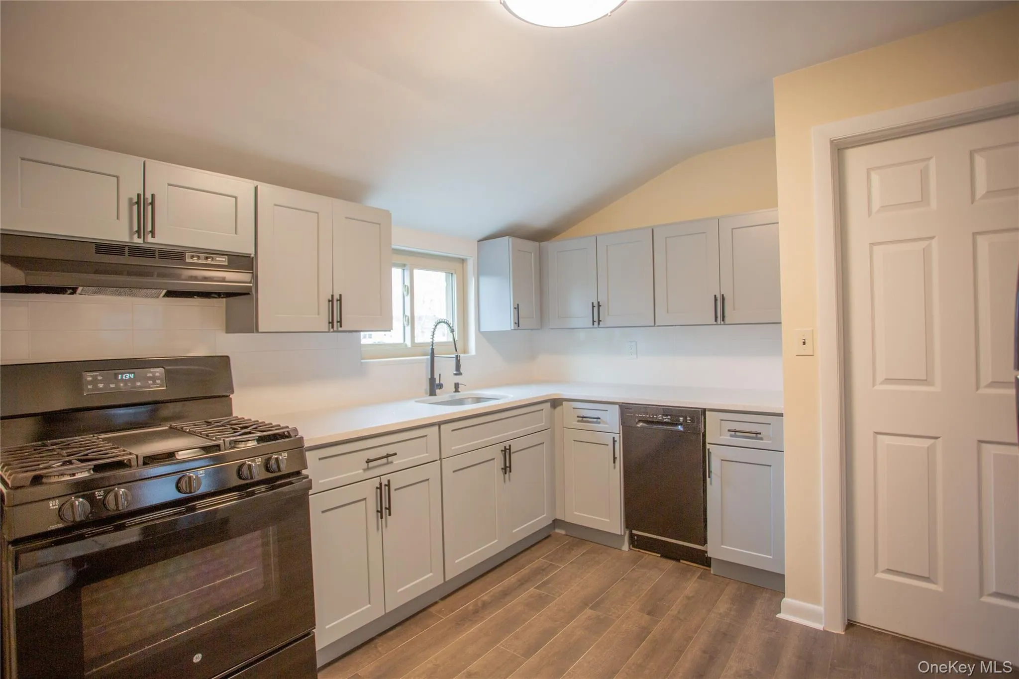 Kitchen with black appliances, lofted ceiling, under cabinet range hood, light countertops, and dark wood-type flooring Kitchen with black appliances, lofted ceiling, under cabinet range hood, light countertops, and dark wood-type flooring