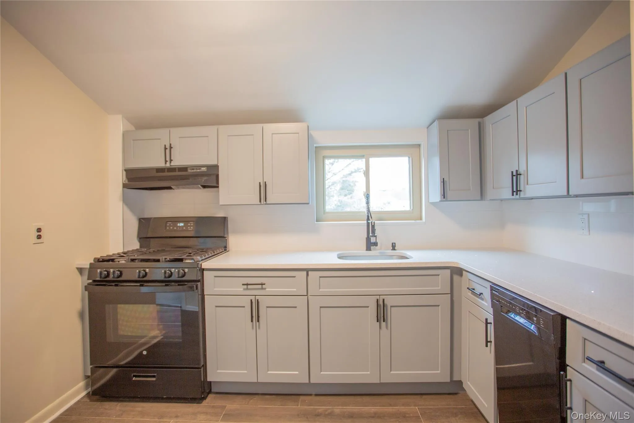 Kitchen with black appliances, wood tiled floors, under cabinet range hood, backsplash, and light stone counters Kitchen with black appliances, wood tiled floors, under cabinet range hood, backsplash, and light stone counters