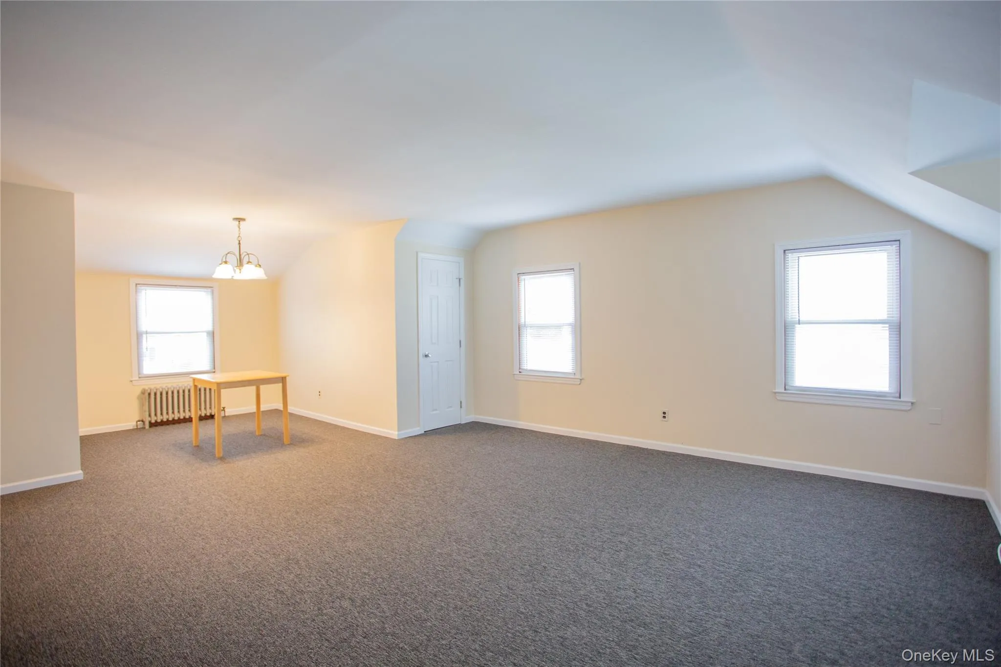 Unfurnished room featuring vaulted ceiling, healthy amount of natural light, radiator heating unit, a chandelier, and dark carpet Unfurnished room featuring vaulted ceiling, healthy amount of natural light, radiator heating unit, a chandelier, and dark carpet