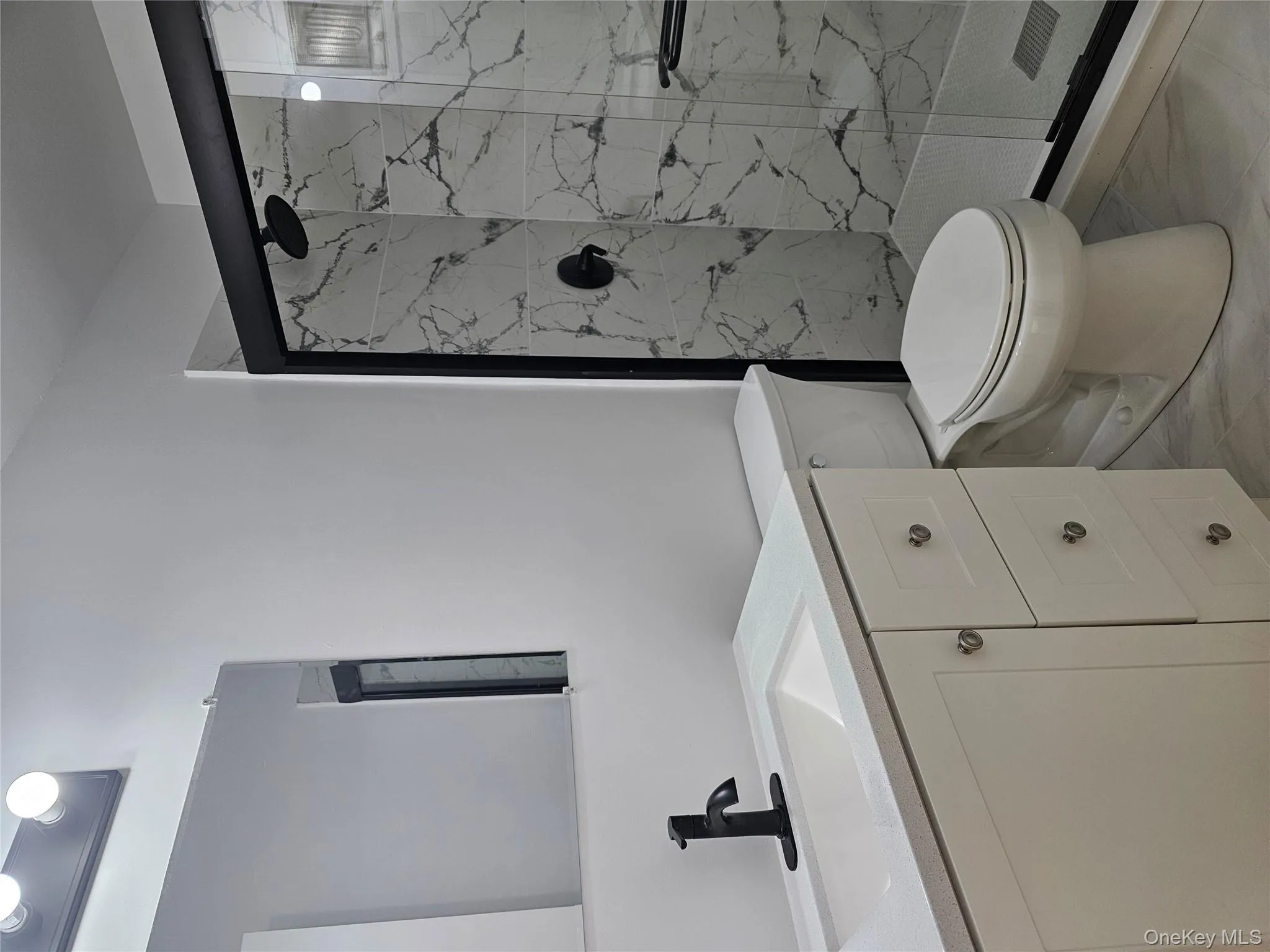 Full bathroom featuring light marble finish floors, vanity, and a marble finish shower Full bathroom featuring light marble finish floors, vanity, and a marble finish shower