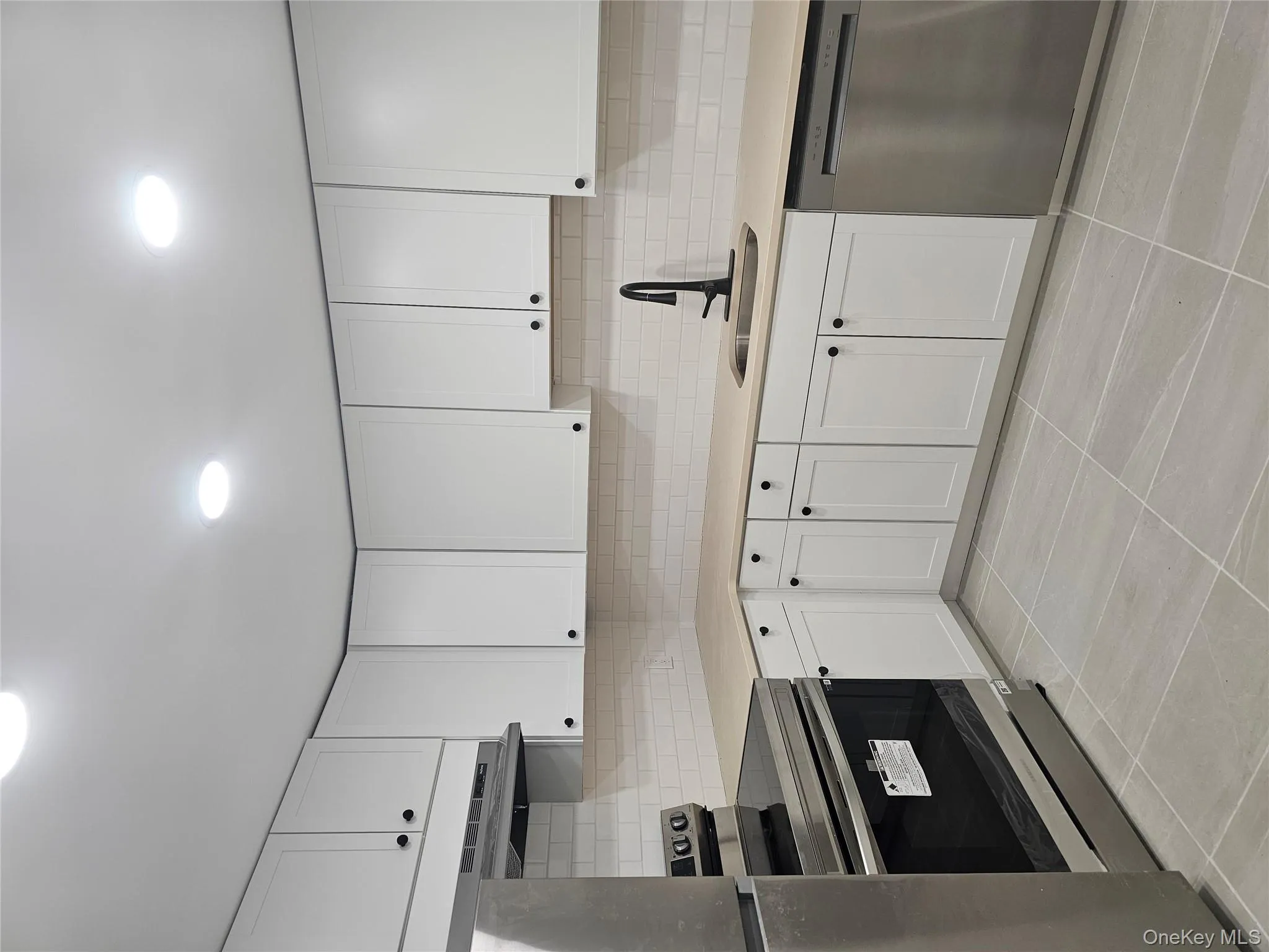 Kitchen with range, dishwasher, white cabinets, backsplash, and light tile patterned floors Kitchen with range, dishwasher, white cabinets, backsplash, and light tile patterned floors