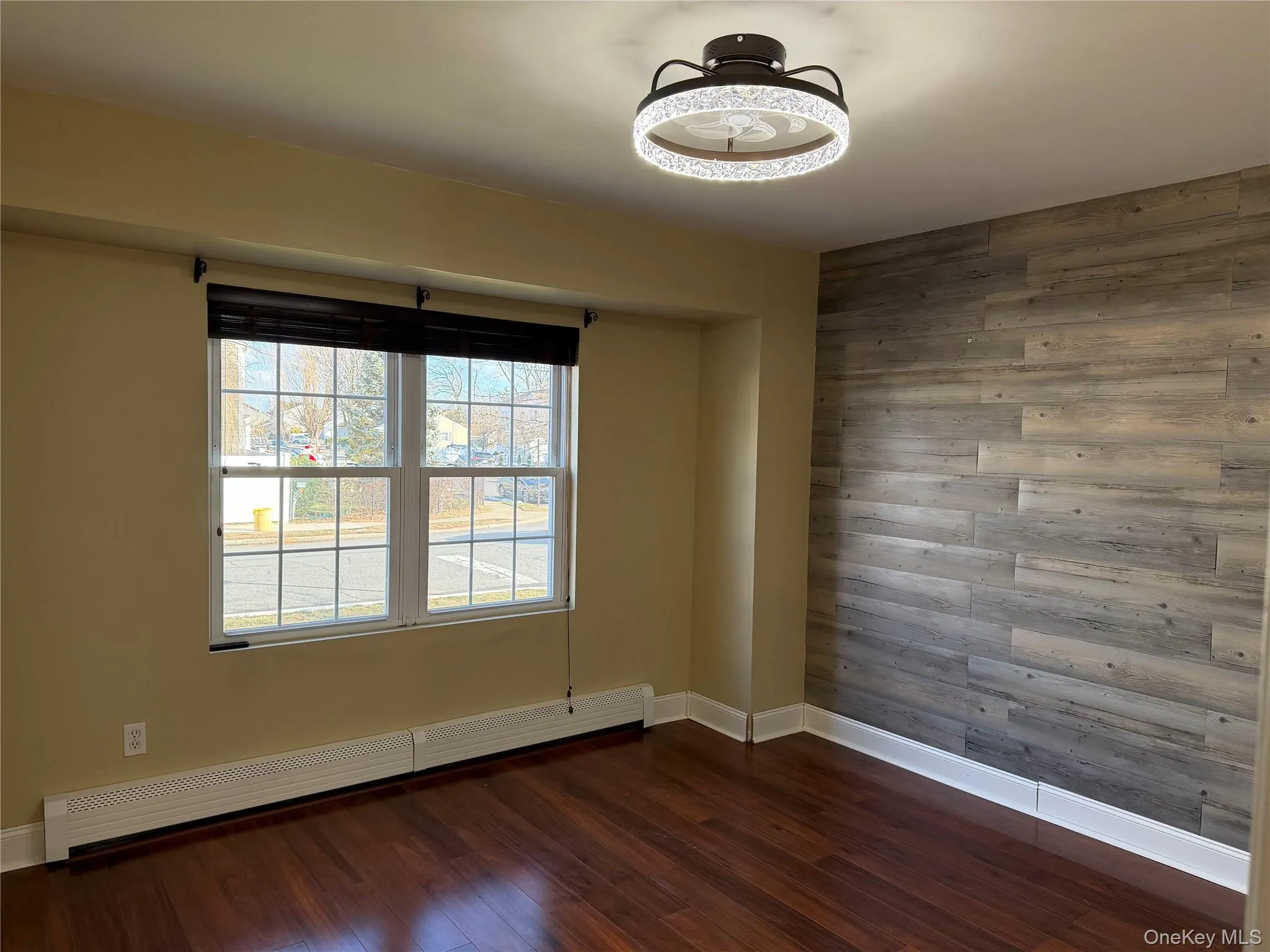 Empty room with wooden walls, a baseboard radiator, dark wood-style flooring, and an accent wall Empty room with wooden walls, a baseboard radiator, dark wood-style flooring, and an accent wall
